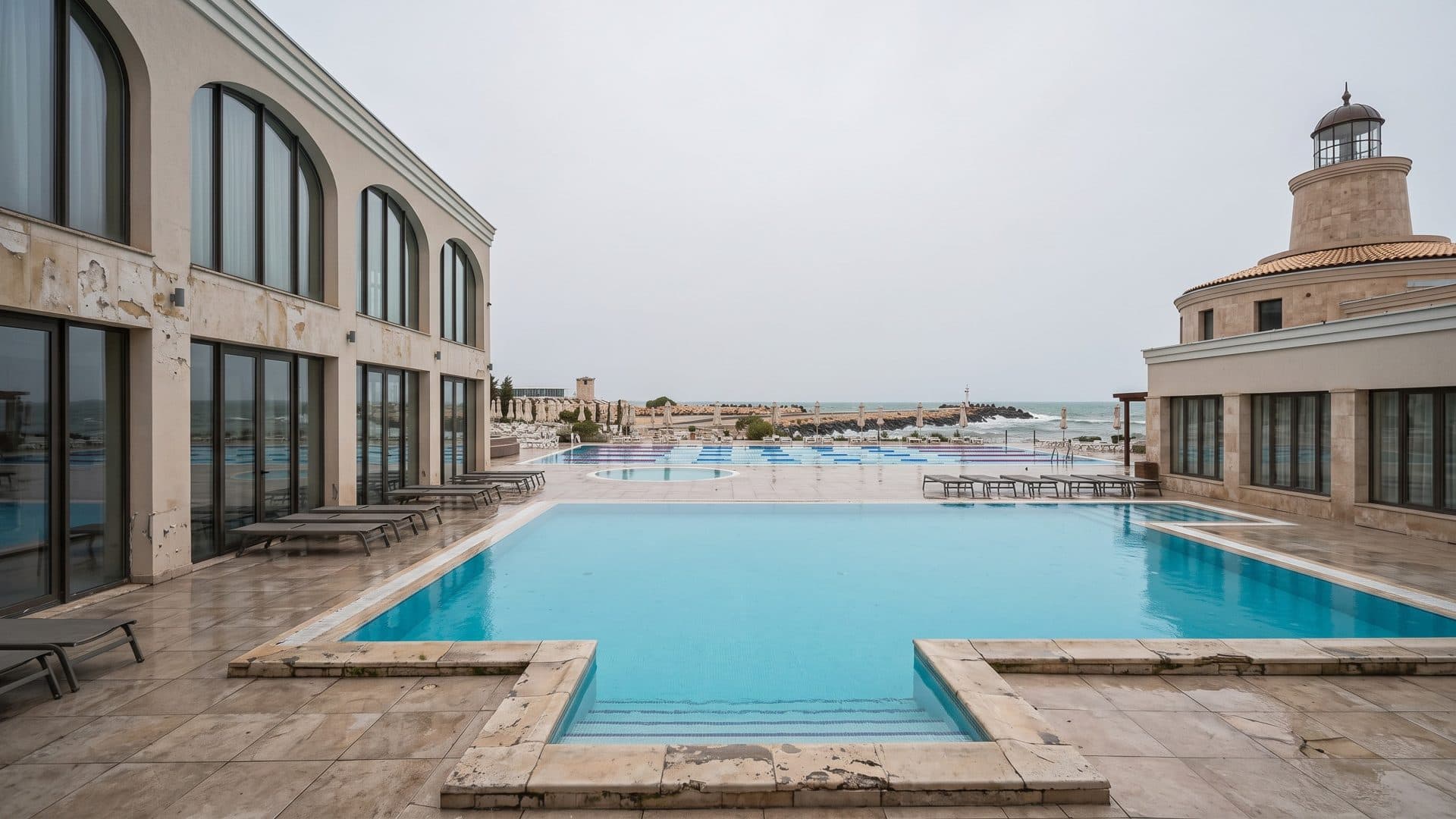 The outdoor pool of the Aqua House spa complex between an arched building and a lighthouse tower by the sea