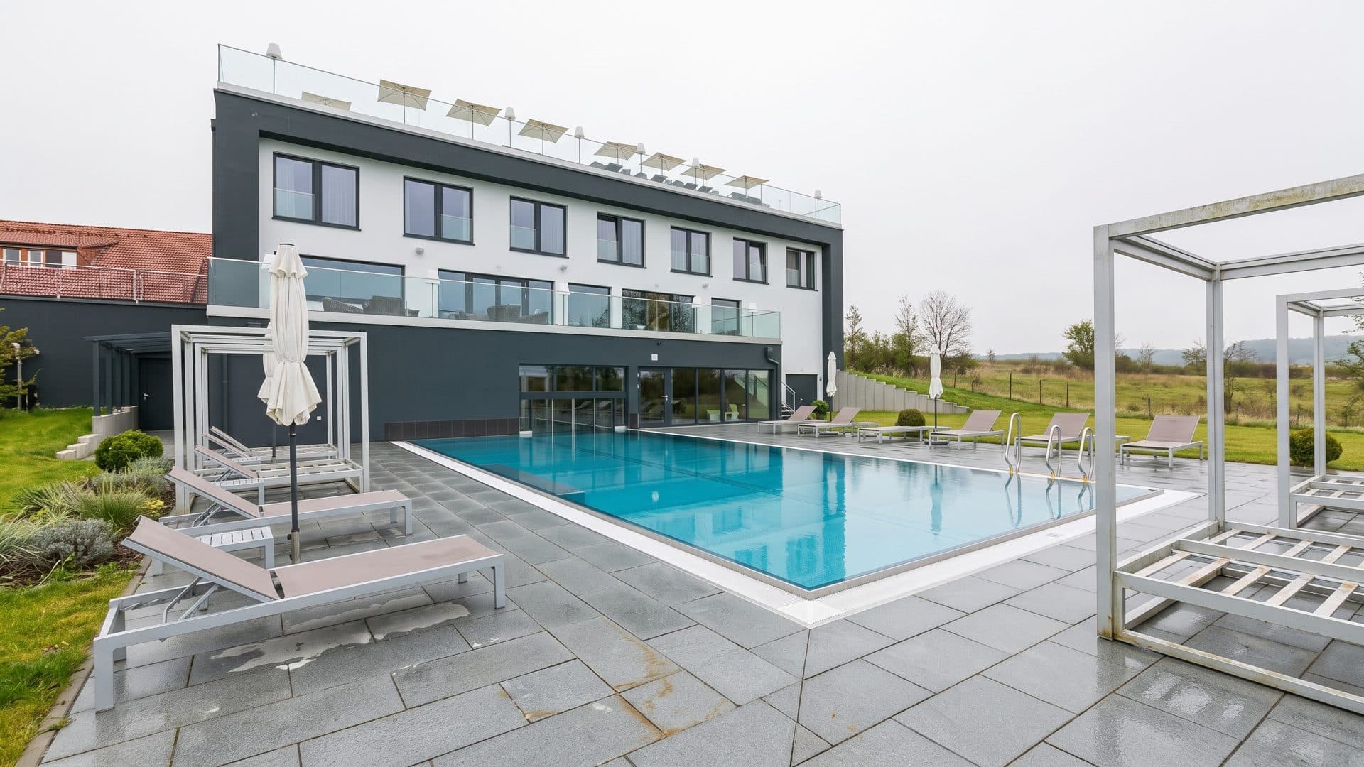 The outdoor pool of SPA Schwanefeld in front of the white hotel building, with loungers and a canopy frame on the terrace