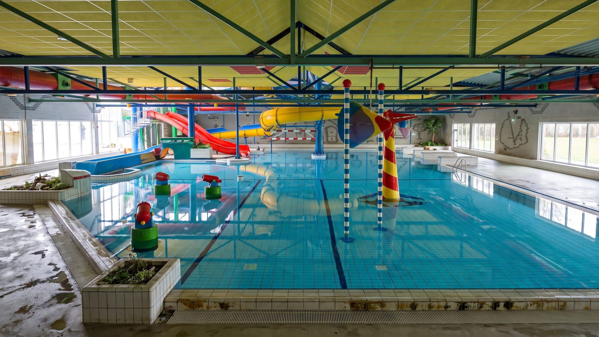 Indoor pool with colourful play columns and water sprayers, and red and yellow slides at the far end