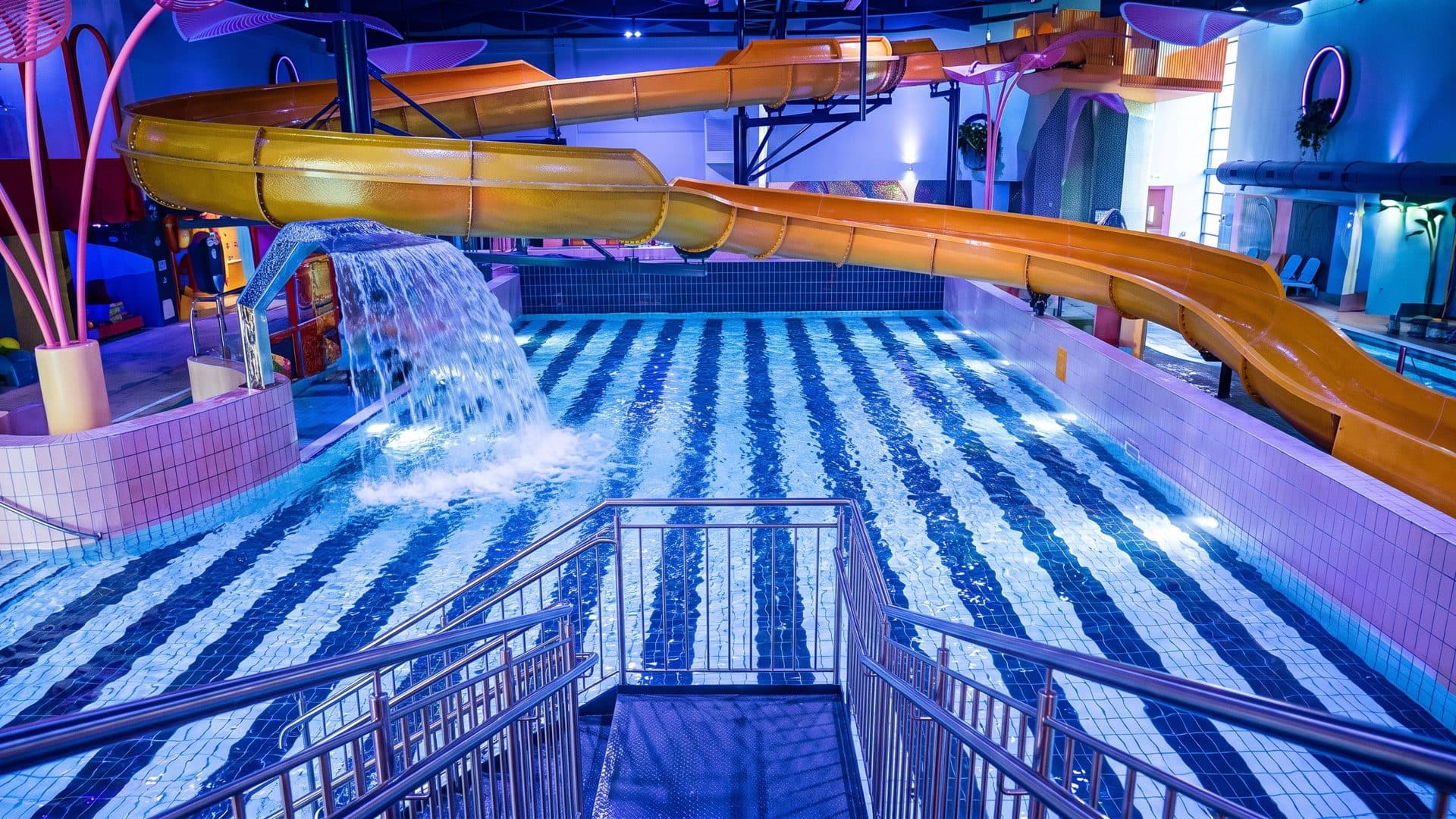 The striped wave pool of Sportiom AquaFun below its orange slide tube and waterfall