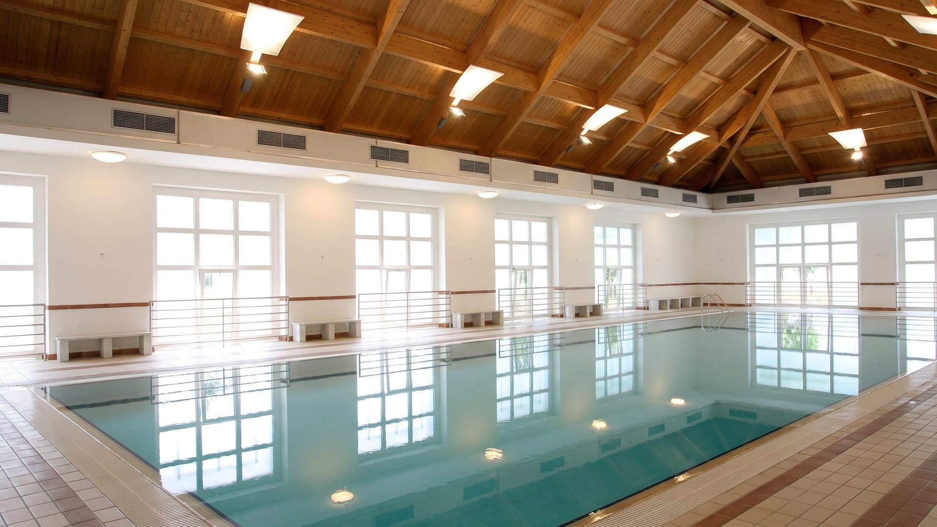 The monumental indoor pool at the Nuove Terme in Acqui Terme, under a timber ceiling between tall windows.