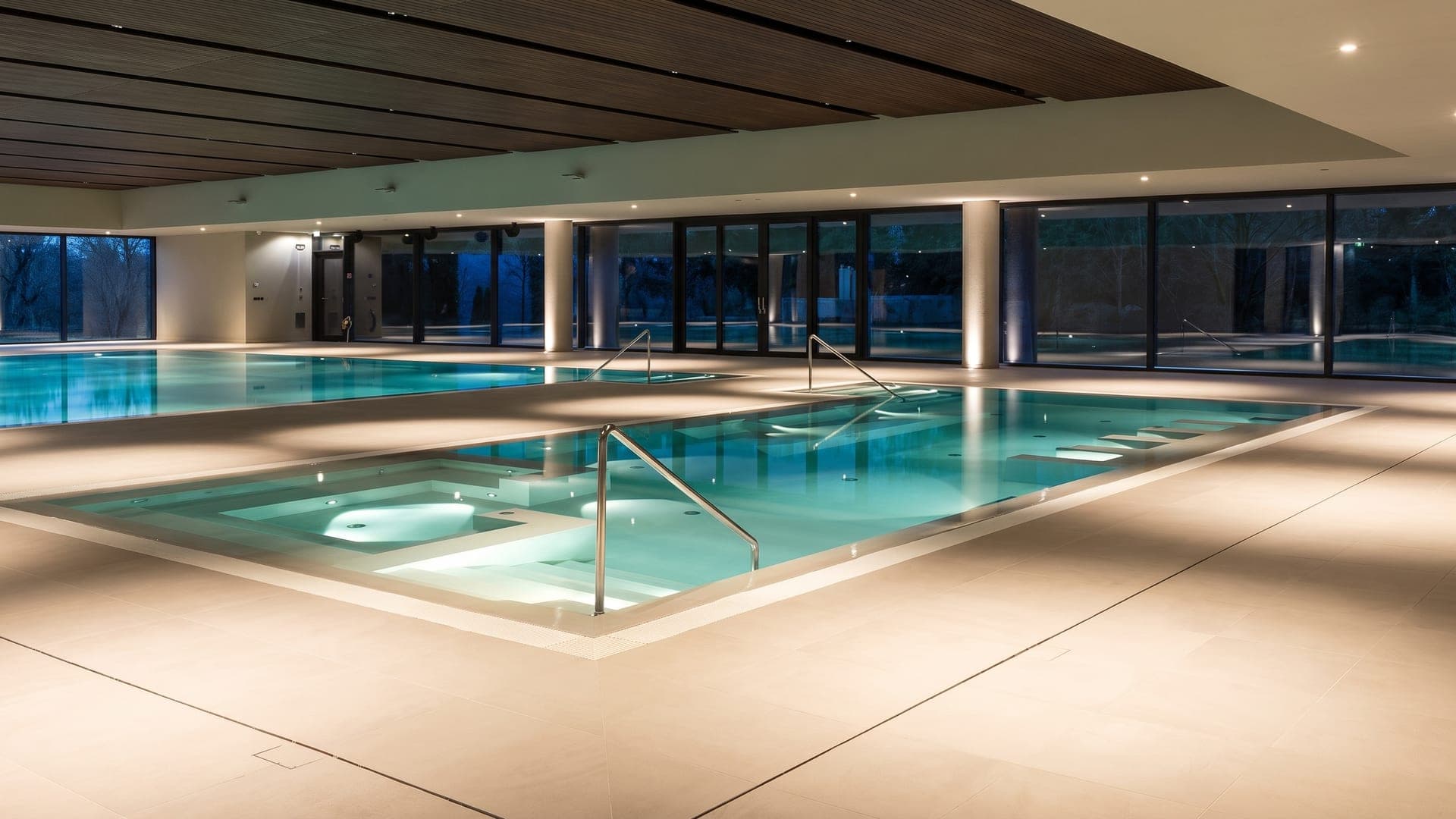 The indoor thermal pool at La Contea in Battaglia Terme, its glass wall opening onto the garden.