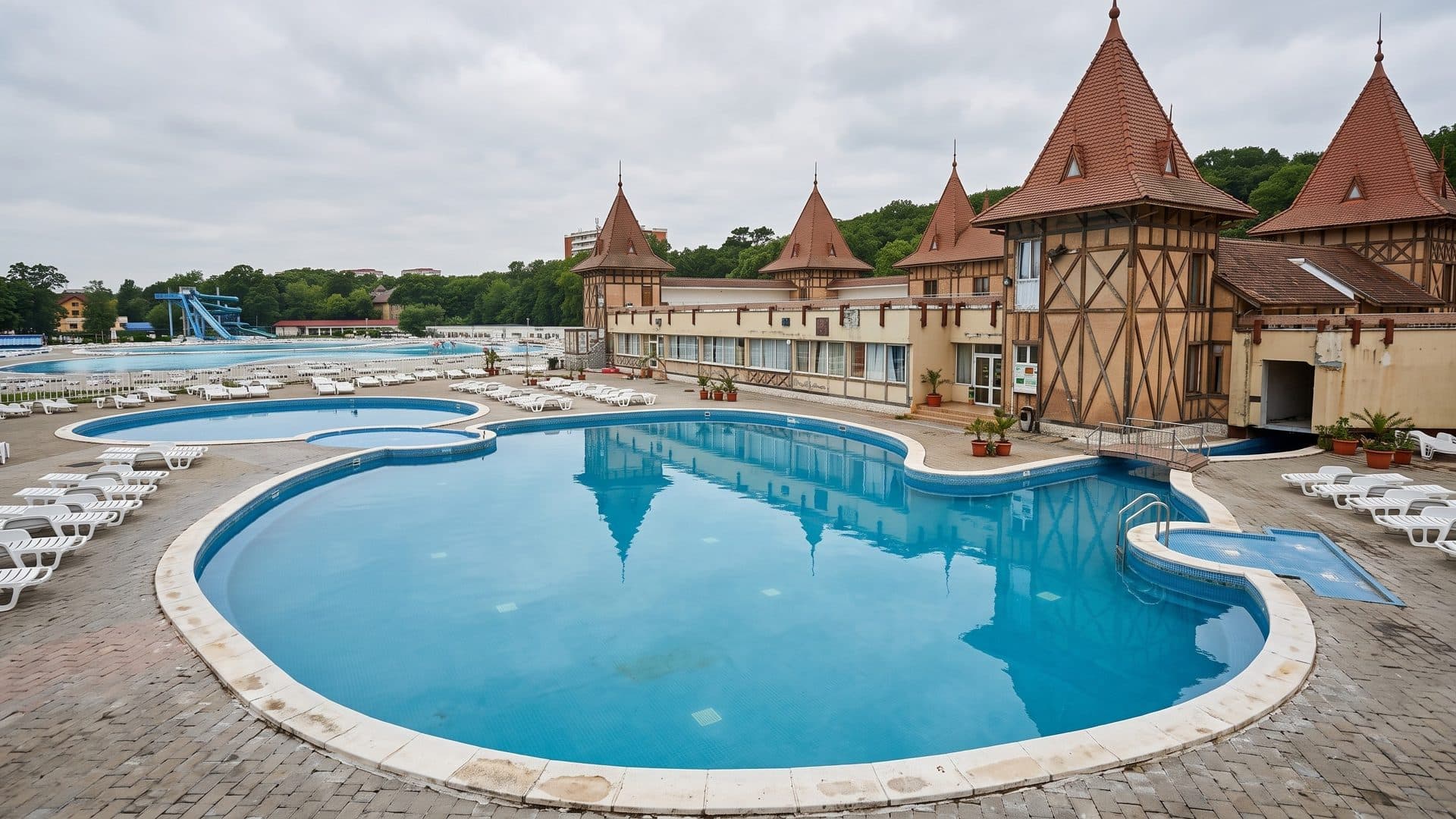 Curved outdoor pools of the Apollo lido in Baile Felix before a building with pointed turrets