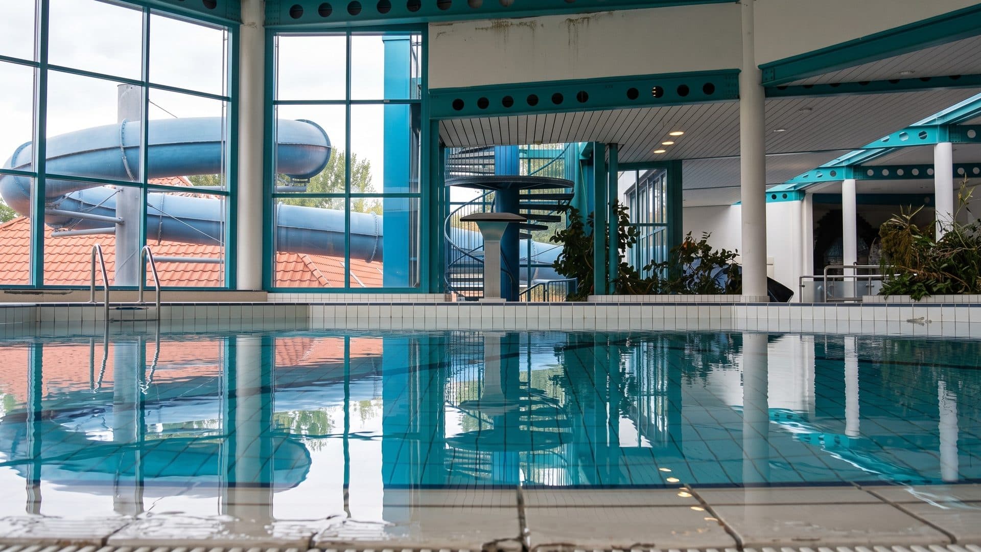 The indoor pool of the Strausbad in Strausberg with turquoise columns and a blue slide behind the glass