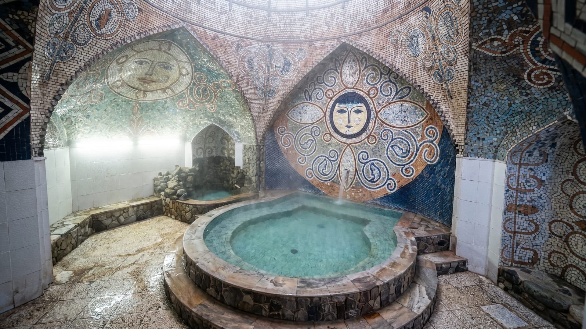 Domed bathing chamber with a round pool, its walls carrying two large sun-face mosaics.