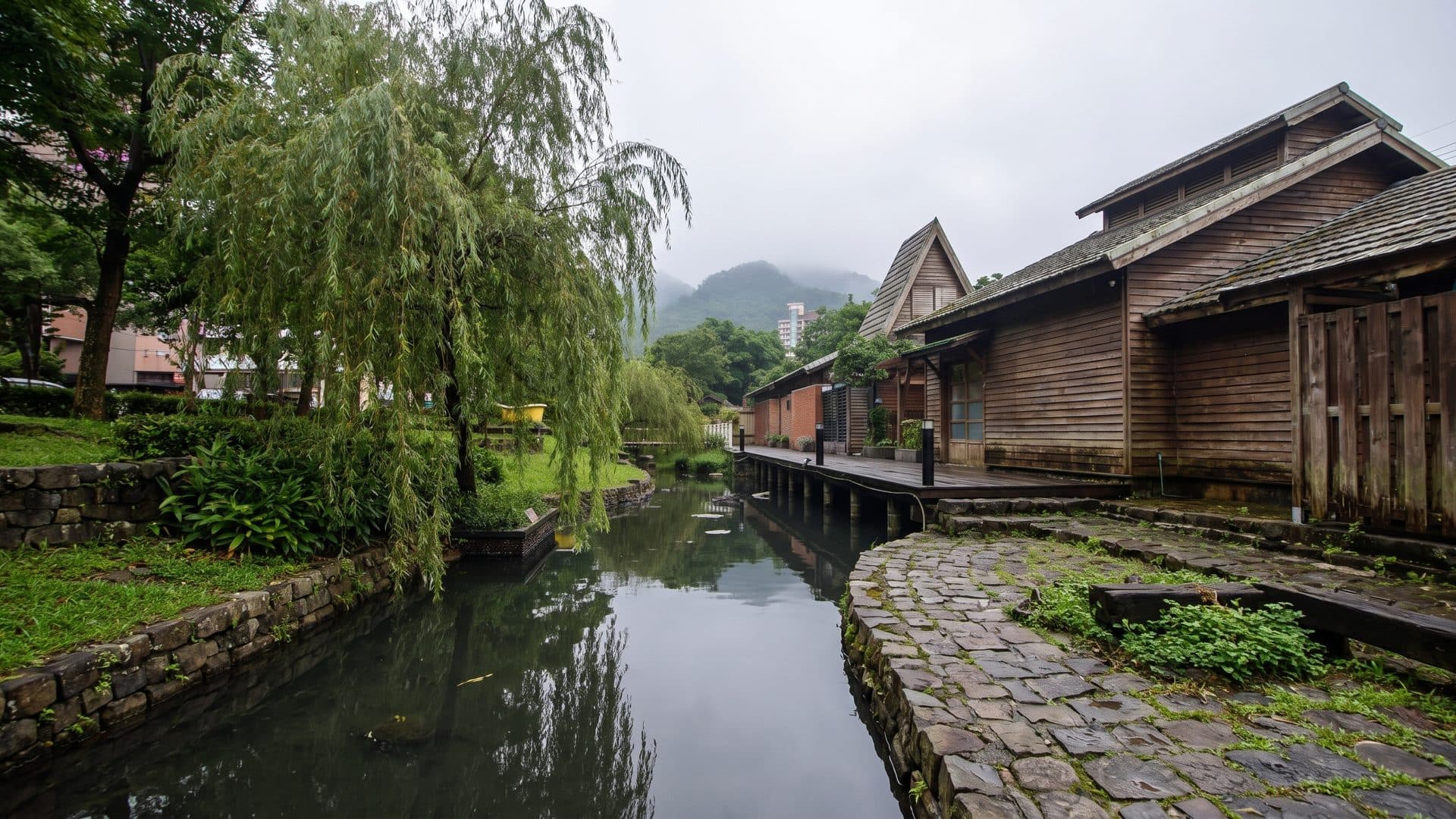 The hot-spring stream at Tangweigou in Jiaoxi running past timber buildings under willows