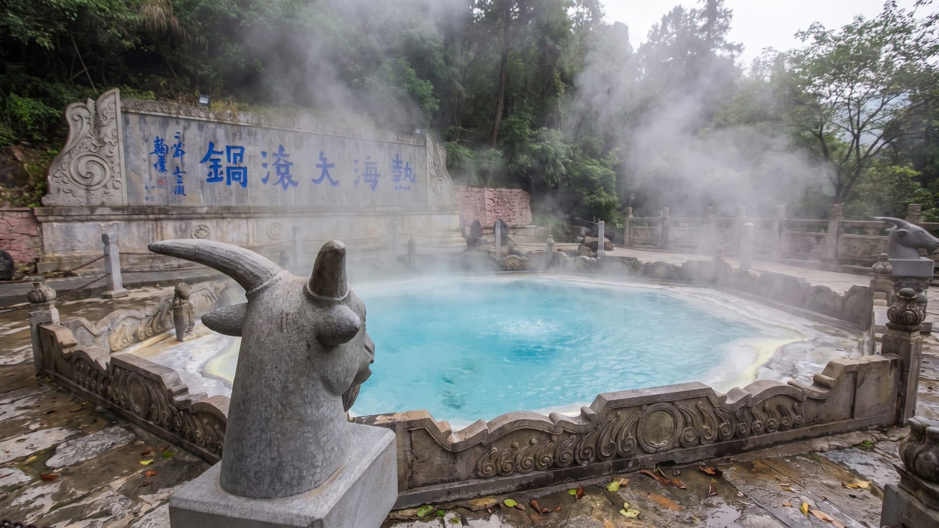 The steaming Big Boiling Pot spring at Tengchong Rehai, with its carved stone animal figure and the inscribed rock wall behind