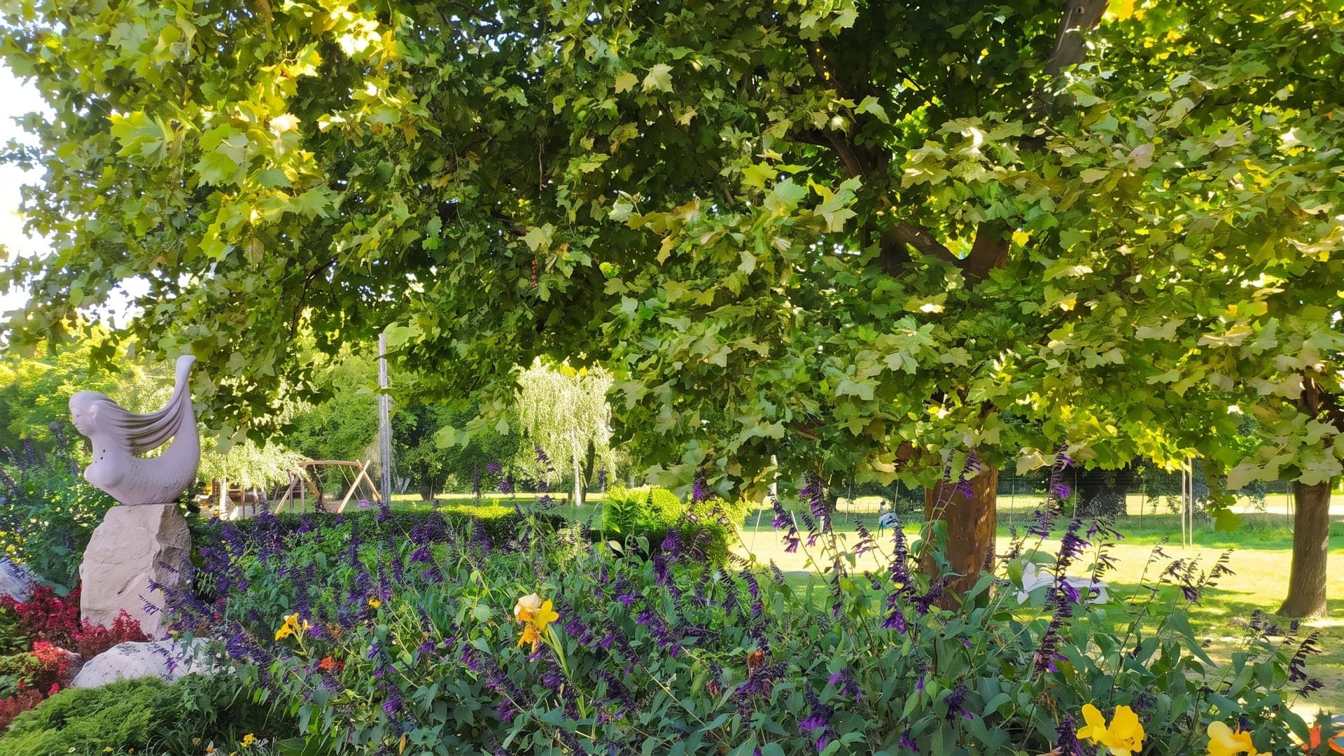 Park with a stone sculpture, a flowerbed and large plane trees