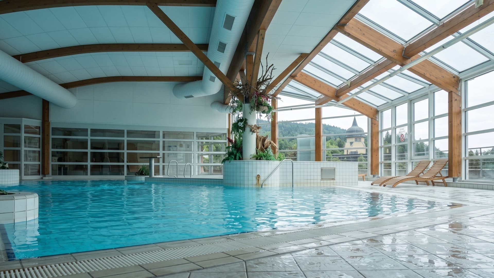 The thermal pool of Janske Lazne under a timber and glass roof, a church tower visible outside