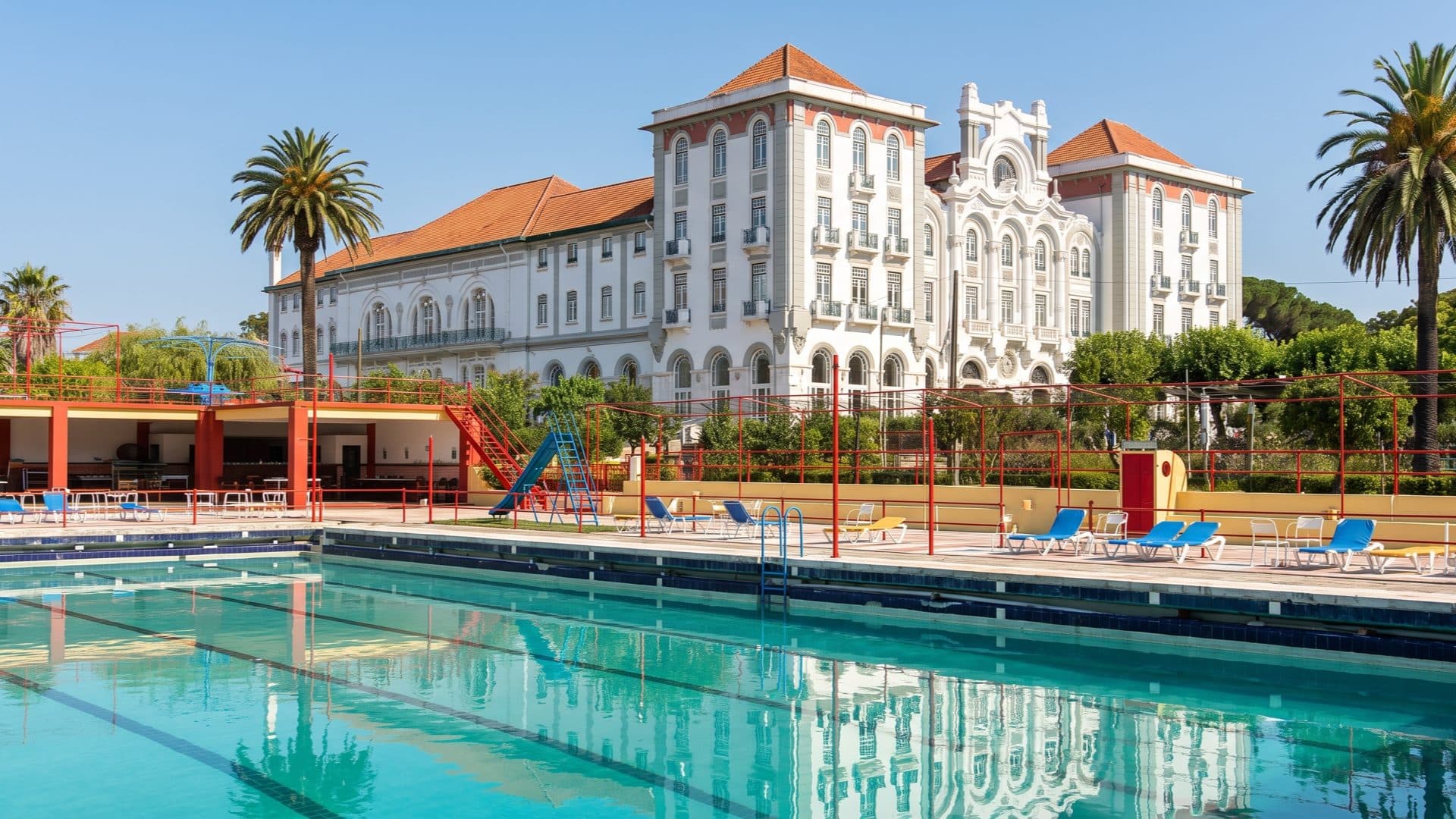 Grand belle-epoque spa hotel with orange-tiled towers rising behind a large rectangular pool and its red diving frames.