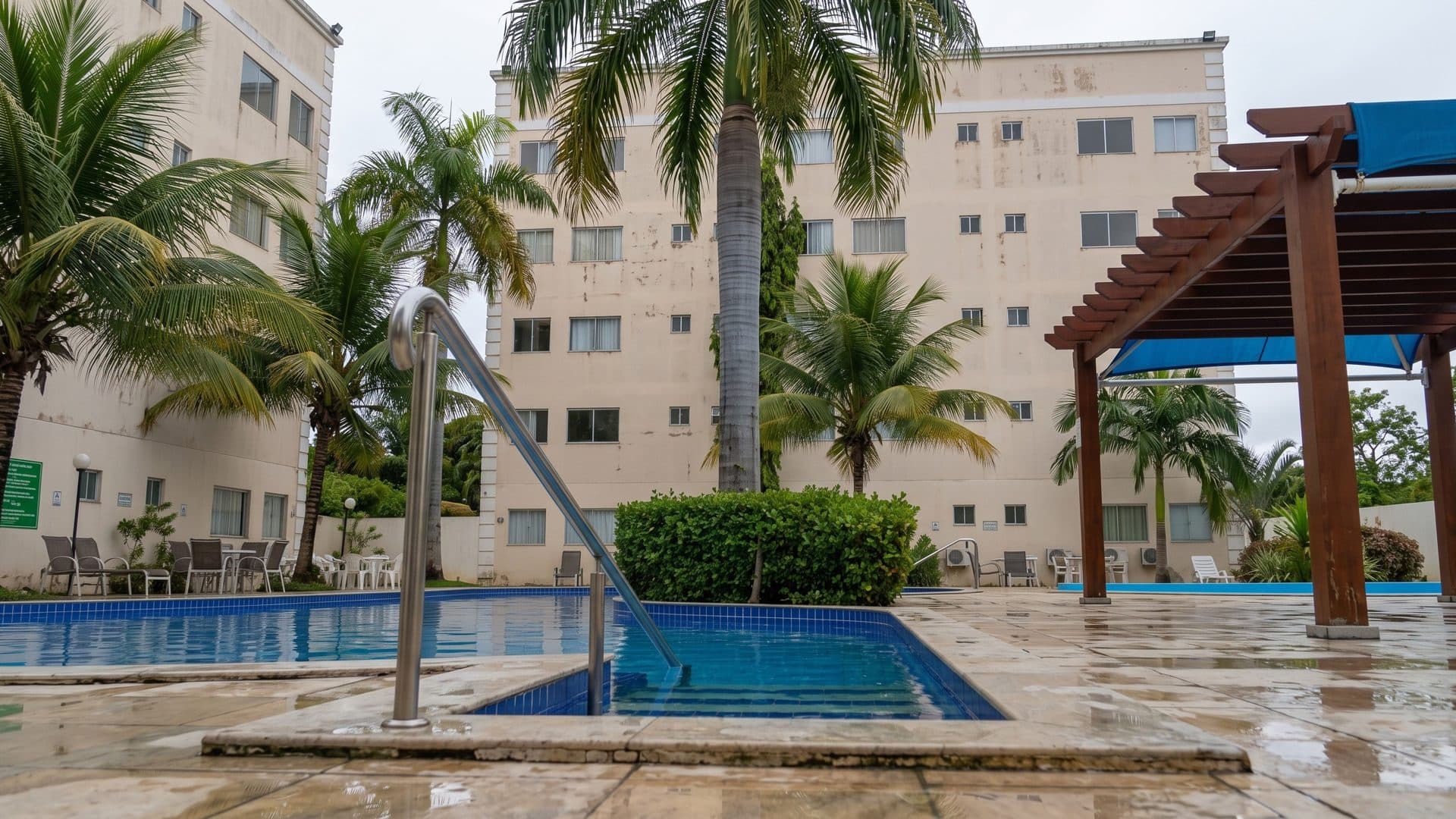 The outdoor pool of Termas das Caldas da Saude among palm trees, with a pergola and the pale hotel blocks behind