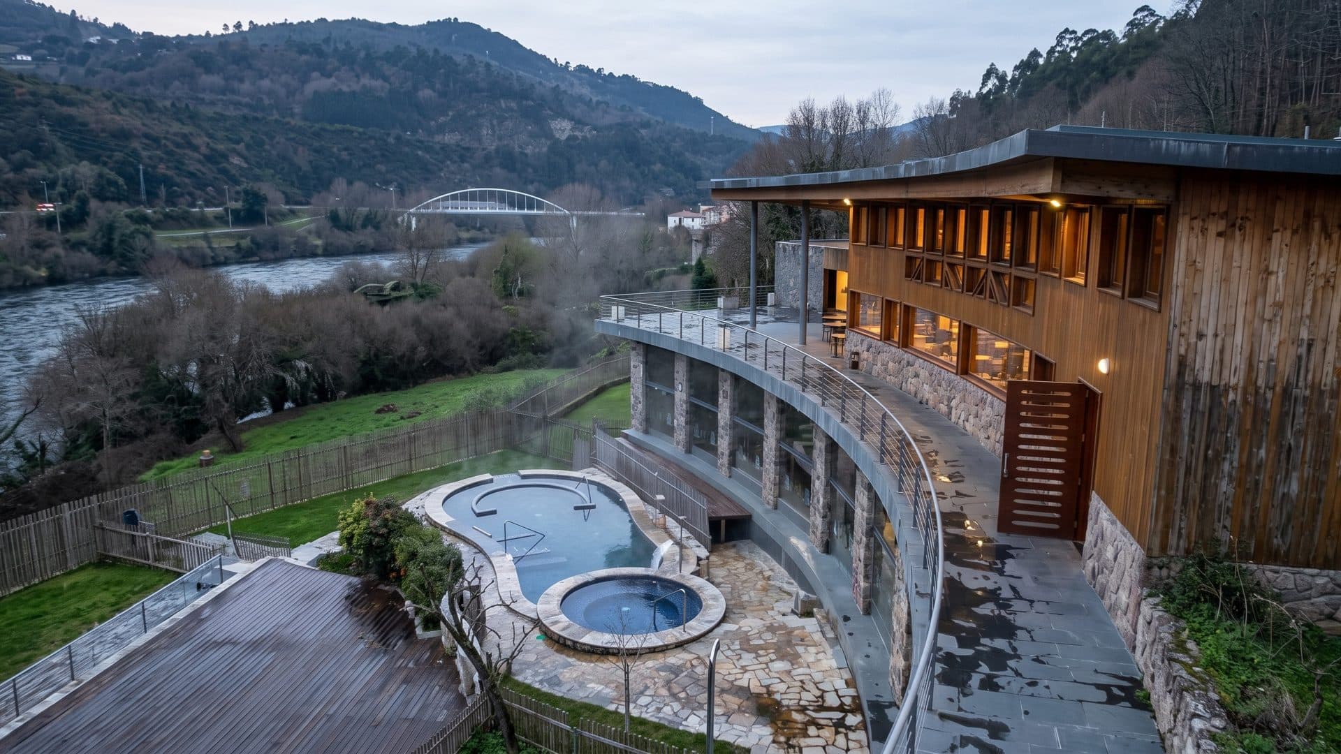The stone thermal pools of Outariz below the curved timber gallery on the bank of the Mino river
