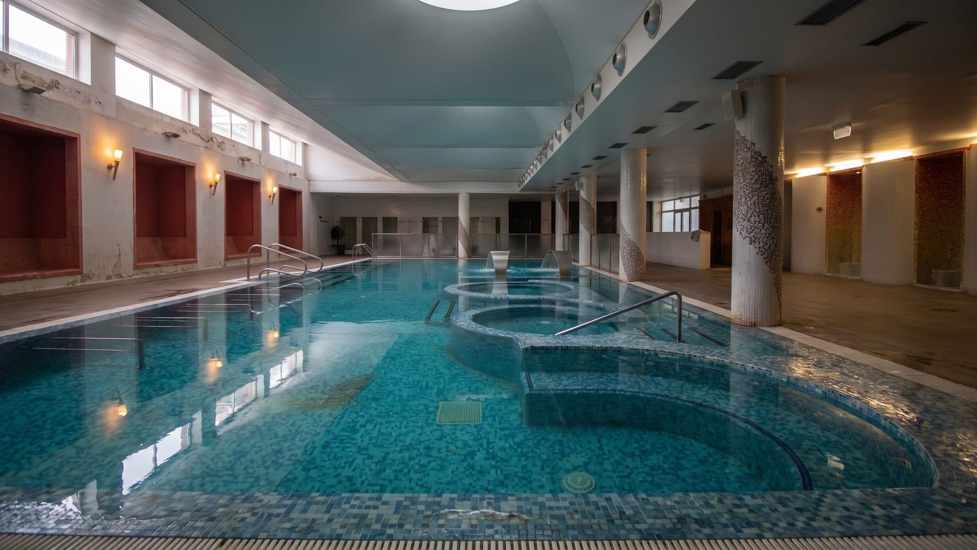 The indoor thermal pool at Sao Vicente under warm lamps, tiled in teal with a shallow basin at one end