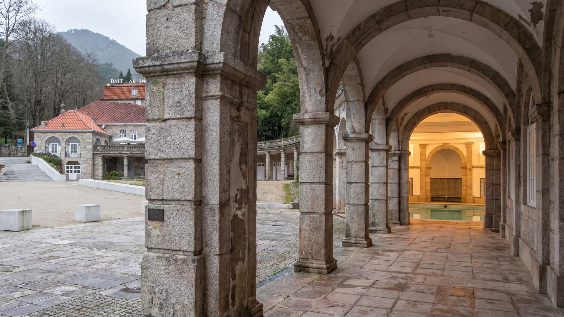 The granite colonnade of the Termas do Geres seen along its arches towards a warmly lit interior at the end