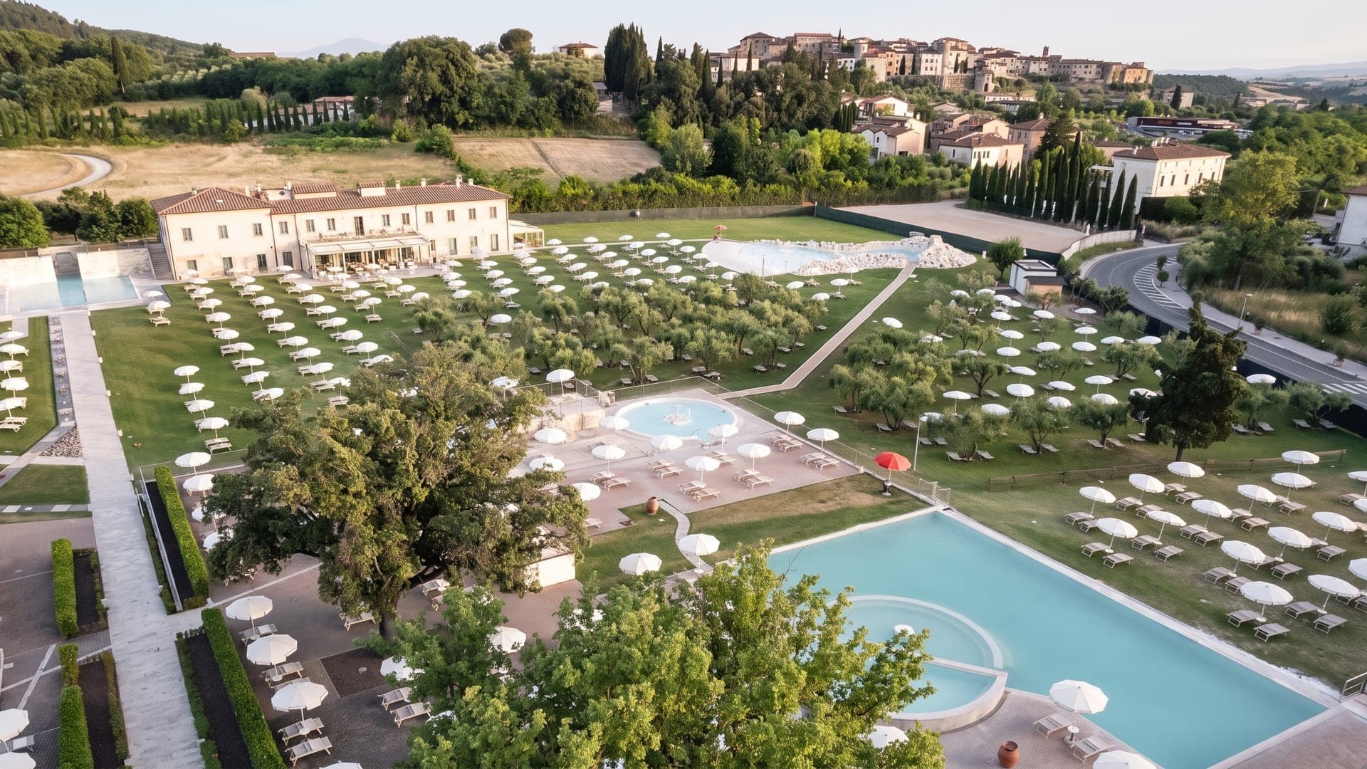 Aerial view of the pools and rows of parasols below the hill town
