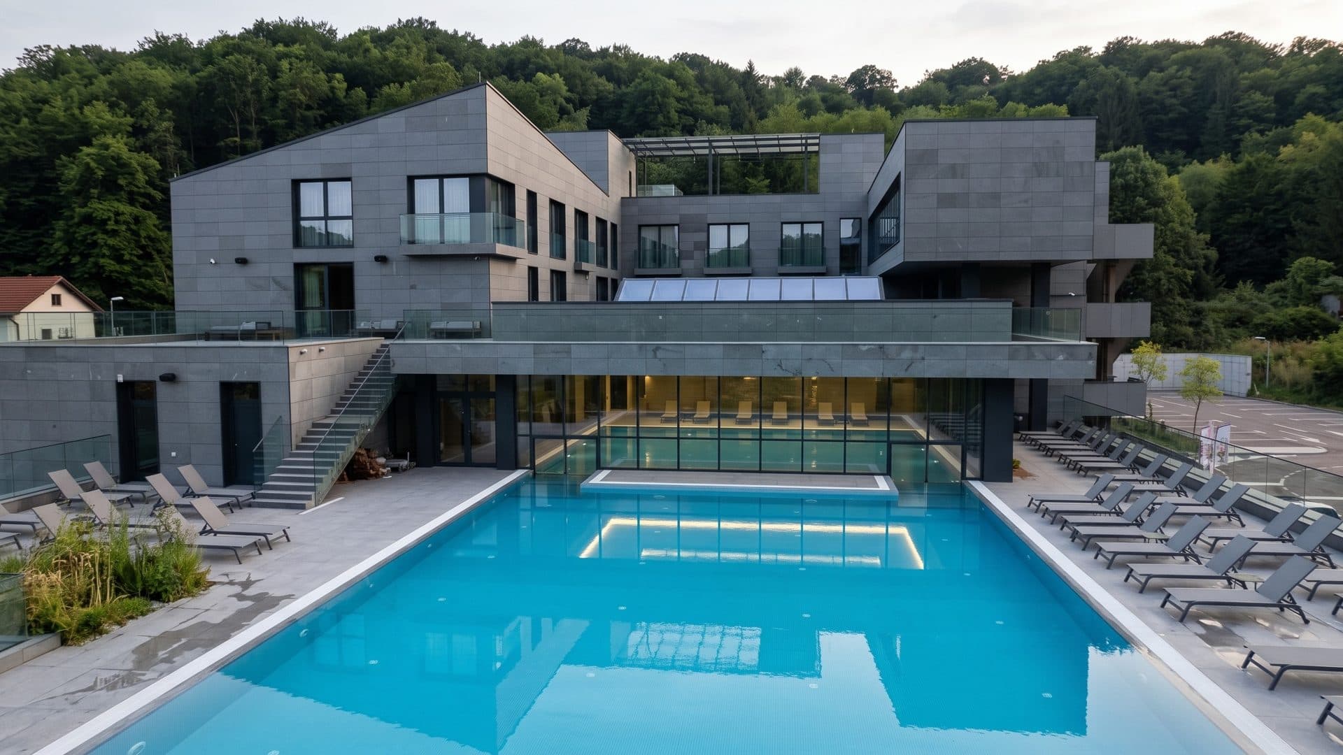 The rectangular outdoor pool of Terme Banja Luka framed by the grey stone building and loungers, wooded hills behind