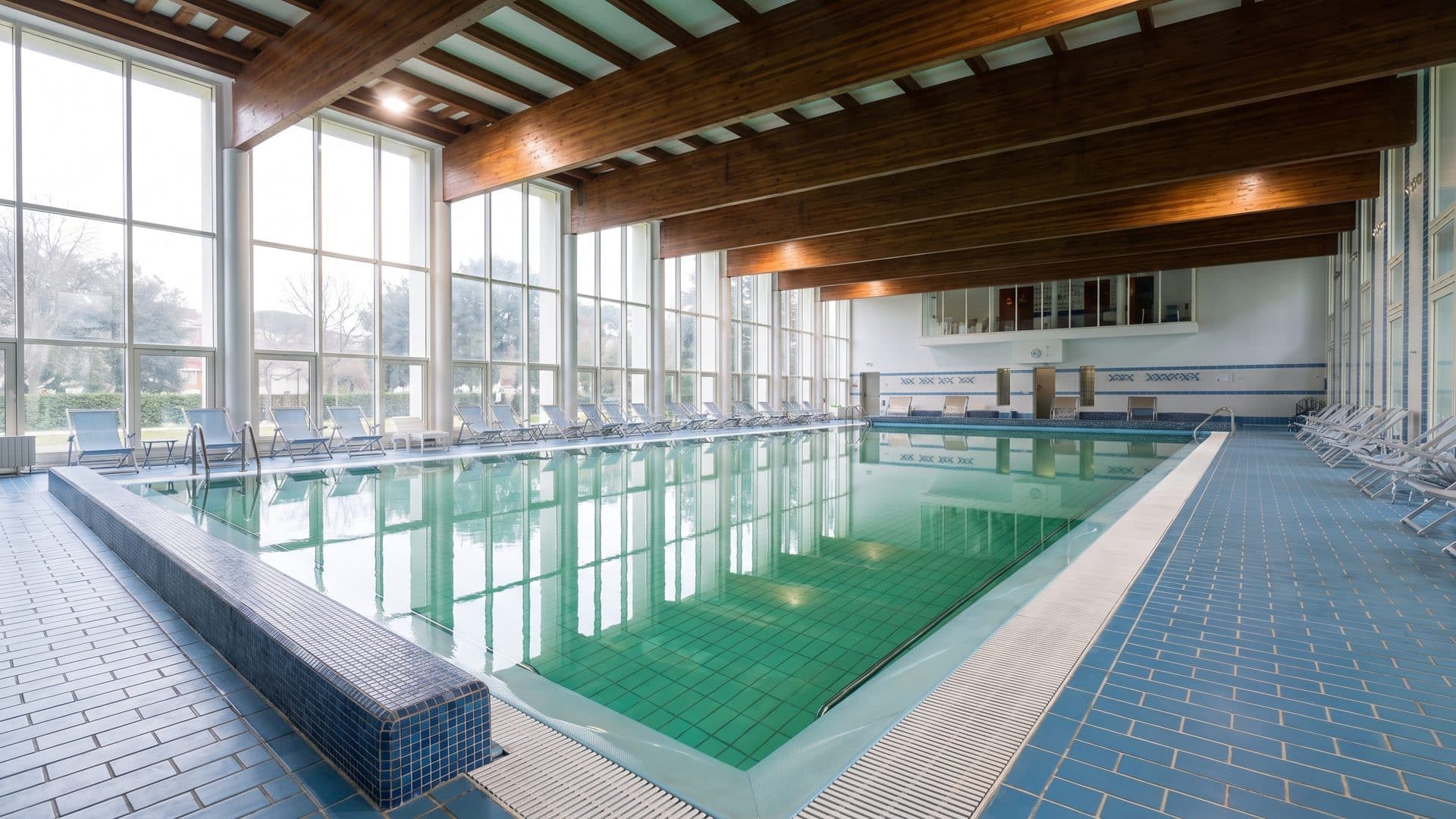 The pool hall at Terme Borrini running towards a full-height glass wall under a timber ceiling