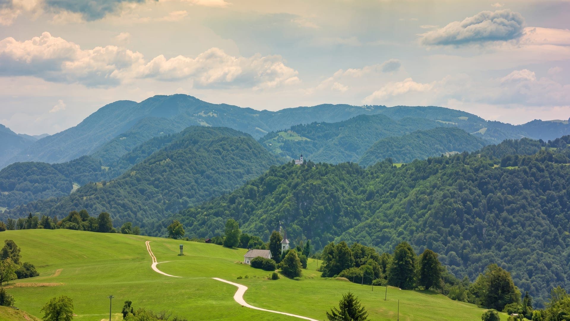 Green meadow and a small church, forested hills beyond