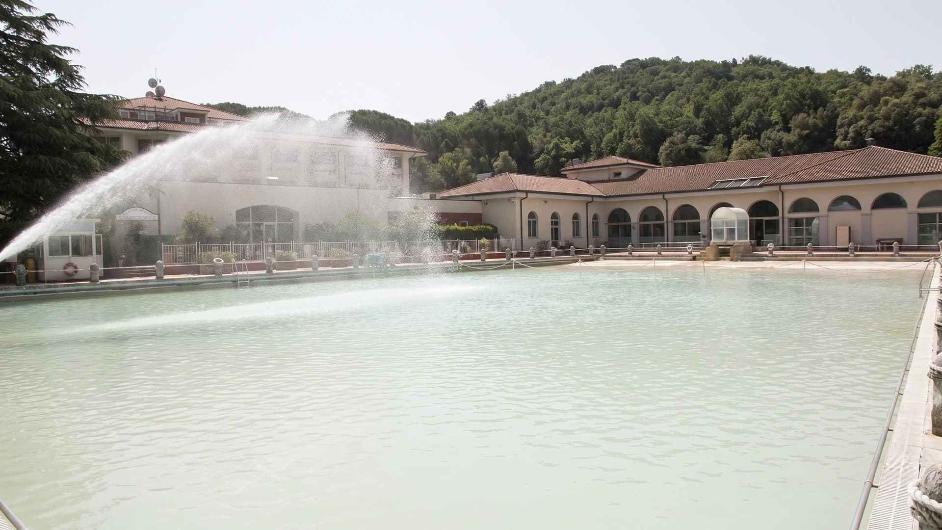 The great thermal pool of Terme dei Papi with its fountain jet and the colonnaded spa building behind