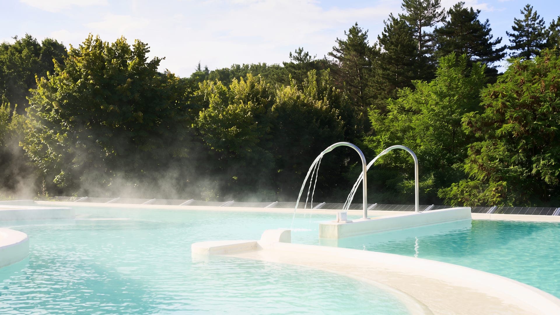Steaming outdoor pool with arched water jets among the trees