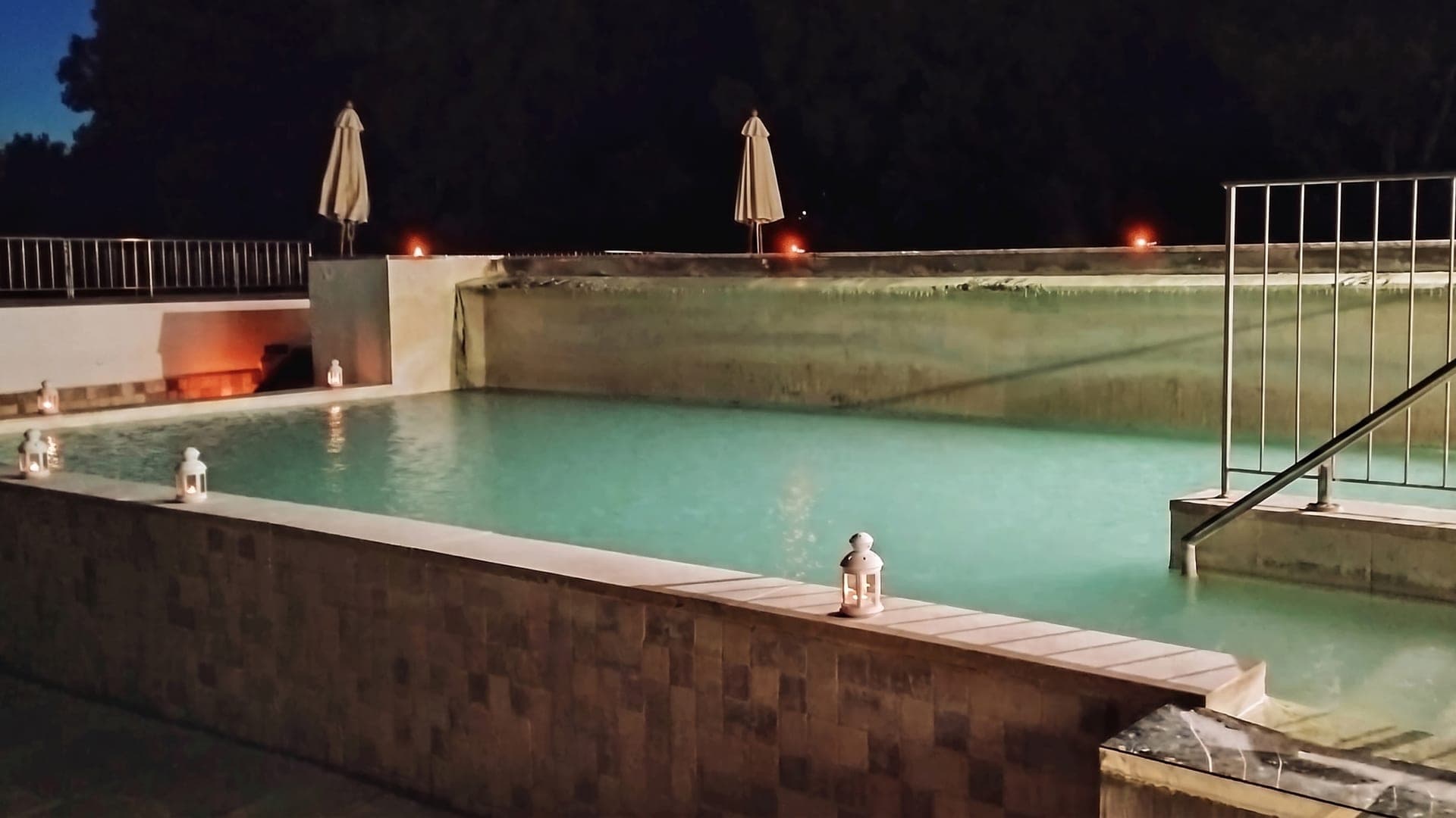 Rectangular pool at dusk, lit by lanterns along the edge