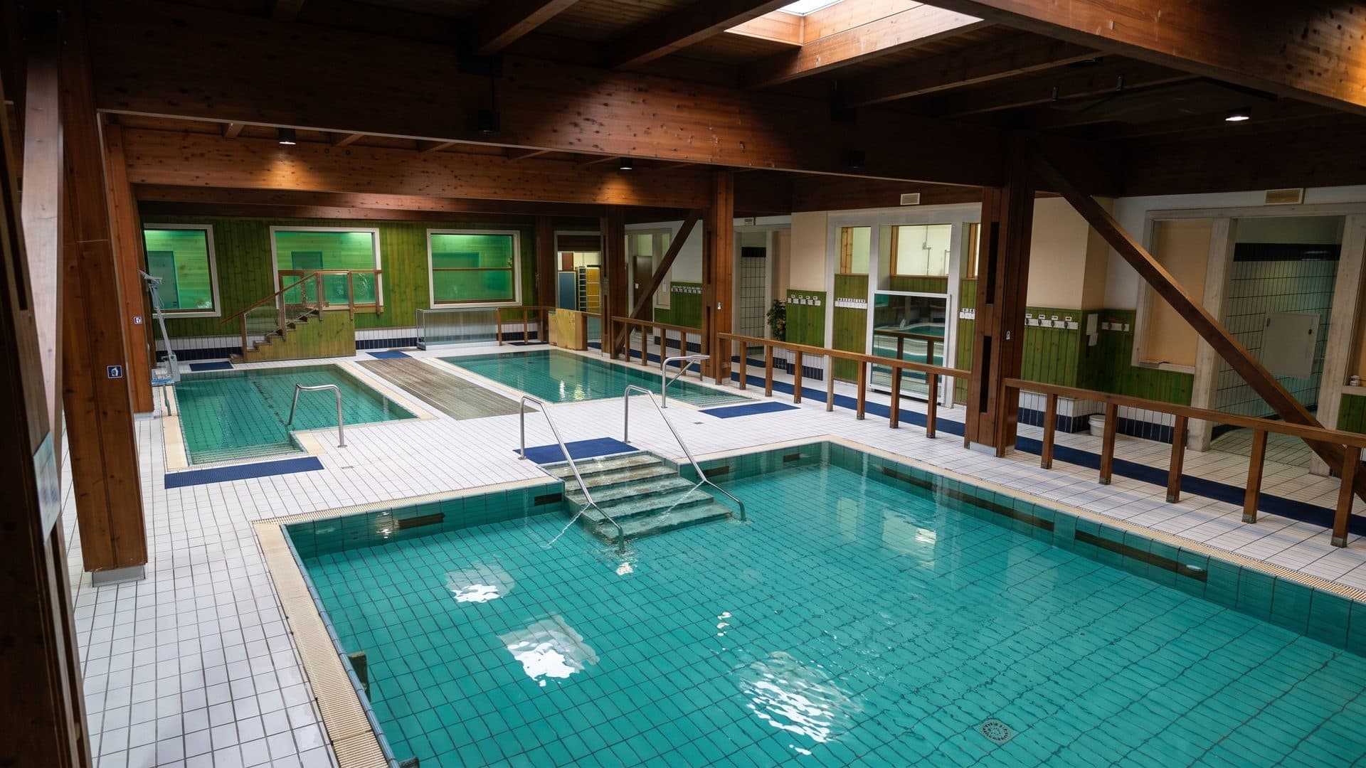 Indoor thermal pools of the Terme di Riccione under a dark timber roof, with green-tiled walls and steps into the water
