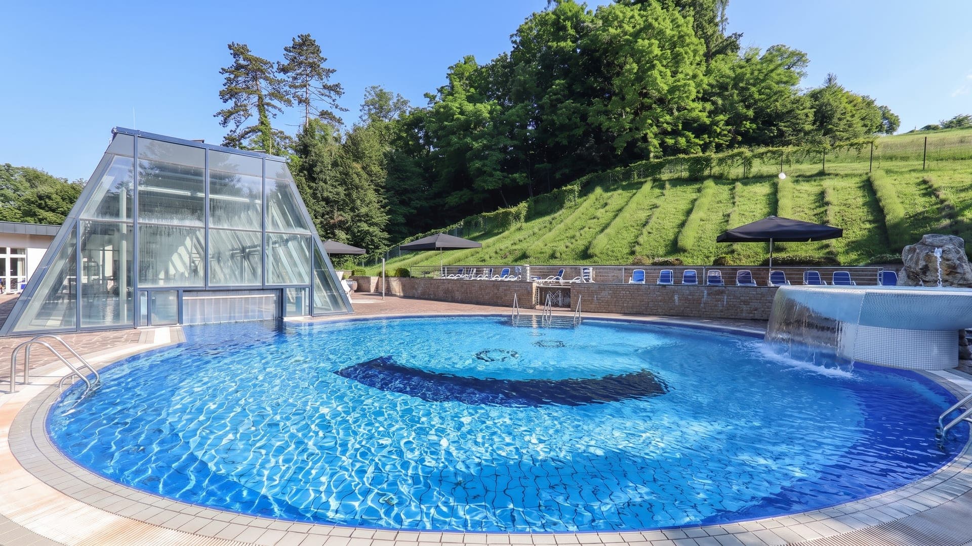 The round outdoor pool at Terme Dobrna, with a terraced green slope rising behind it.