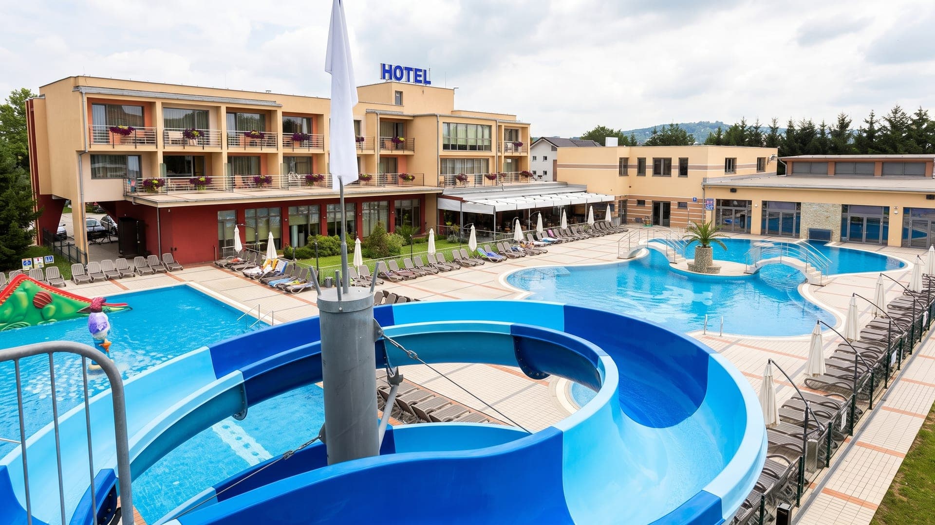 The outdoor pools at Terme Paradiso in Dobova, with a blue waterslide and the hotel behind.
