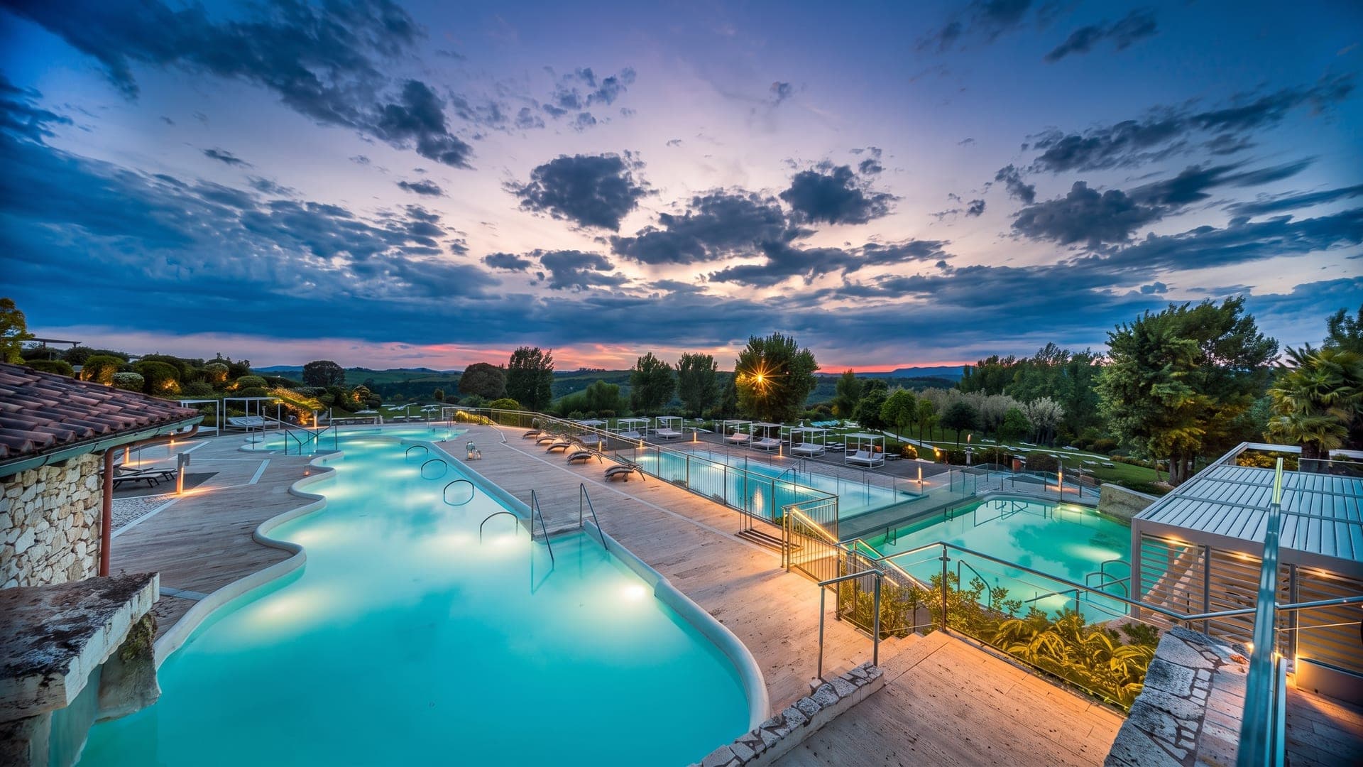 The outdoor pools at Terme San Giovanni in Rapolano under an evening sky, set among stone walls and olive trees.