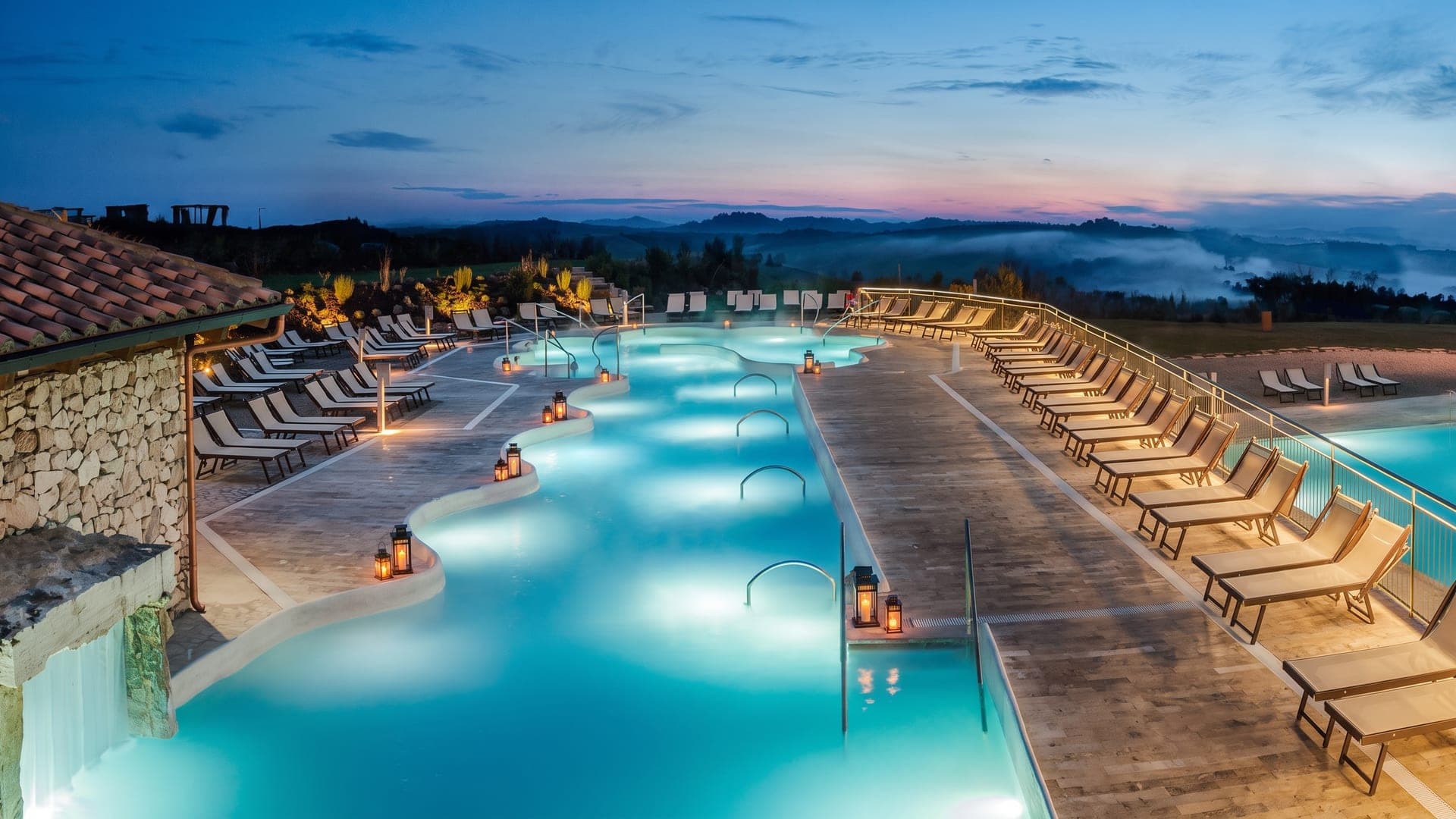 The turquoise pools at Terme San Giovanni in Rapolano at dusk, lanterns along the edge and the Tuscan hills beyond.