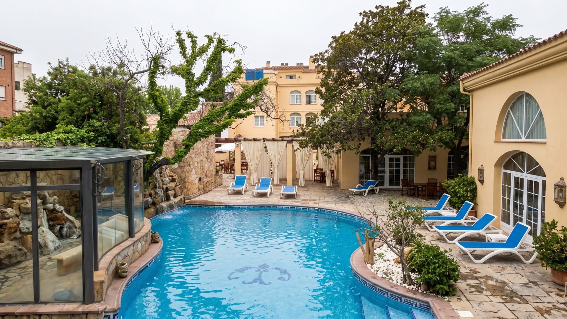 The curved pool in the garden of Termes La Garriga with blue loungers, the arched spa building behind