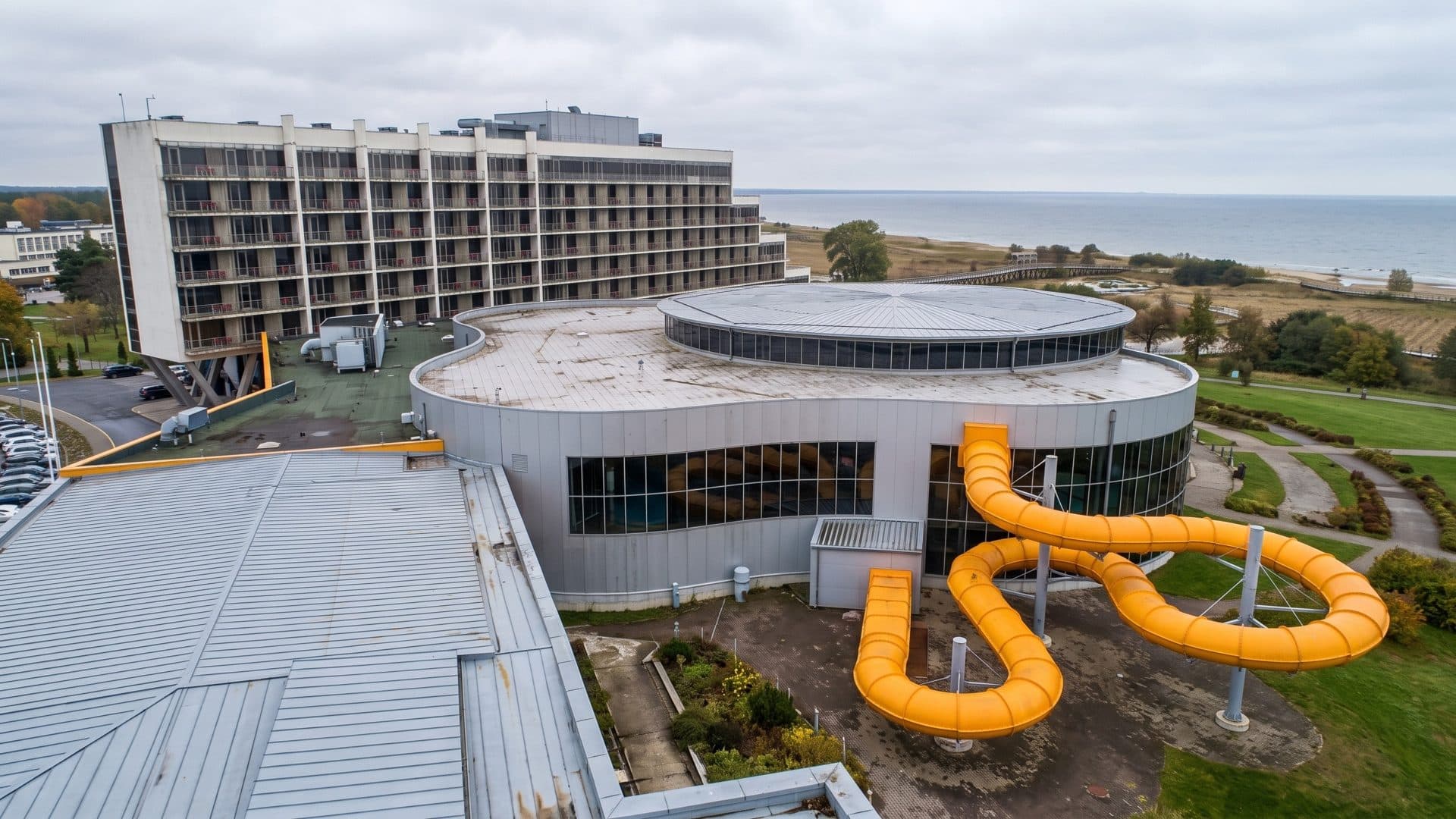 The round Tervise Paradiis water park building in Parnu with a yellow slide outside, the hotel tower and the sea beyond
