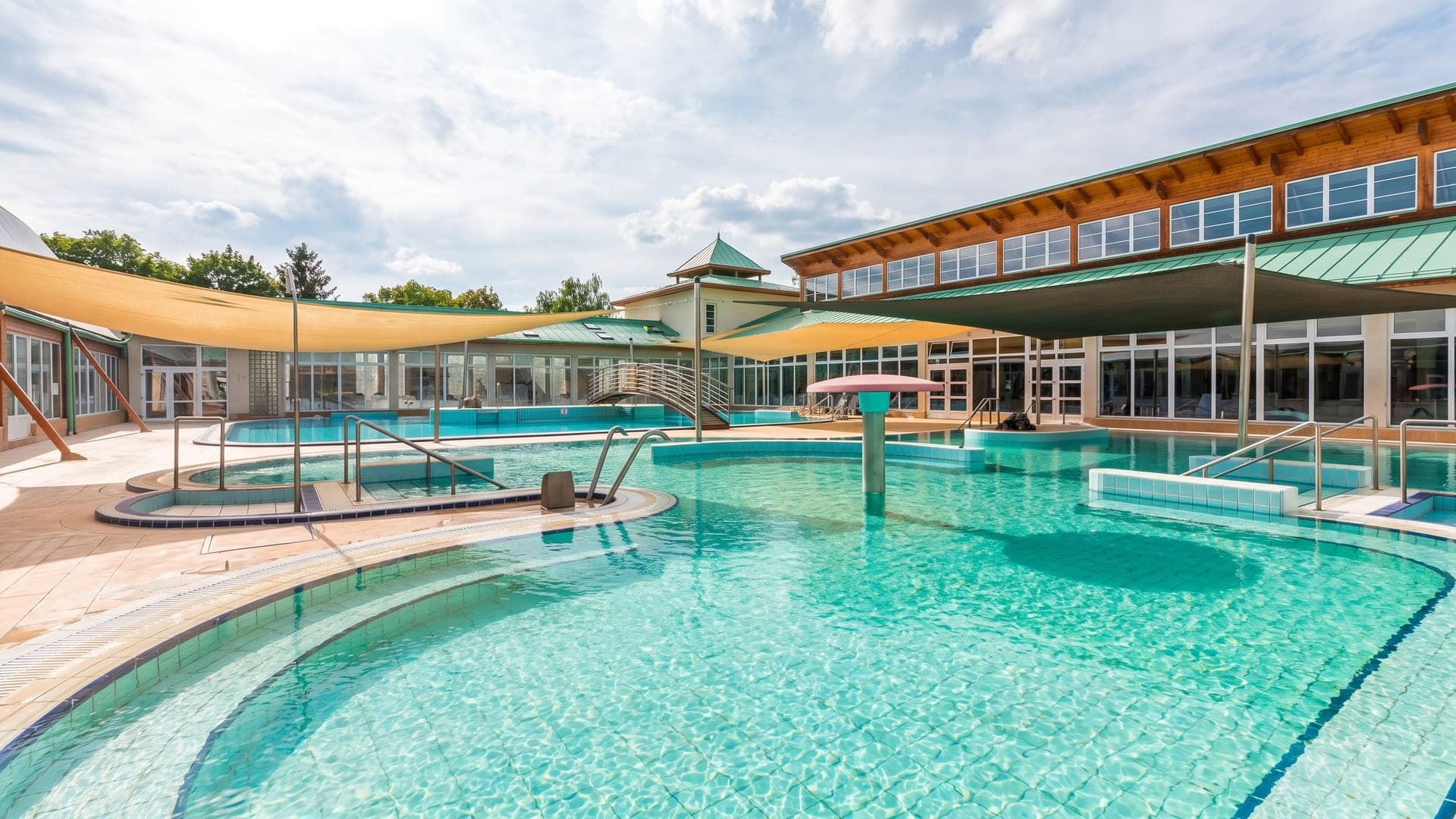 The outdoor pools at the Thermal Spa in Mosonmagyarovar, shaded by sail canopies beside the pagoda-roofed pavilion.