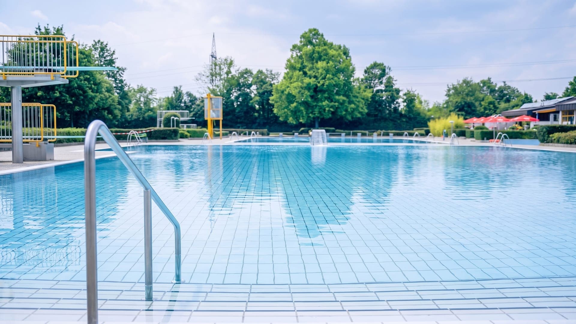 Large outdoor pool with diving platforms, trees along the far side