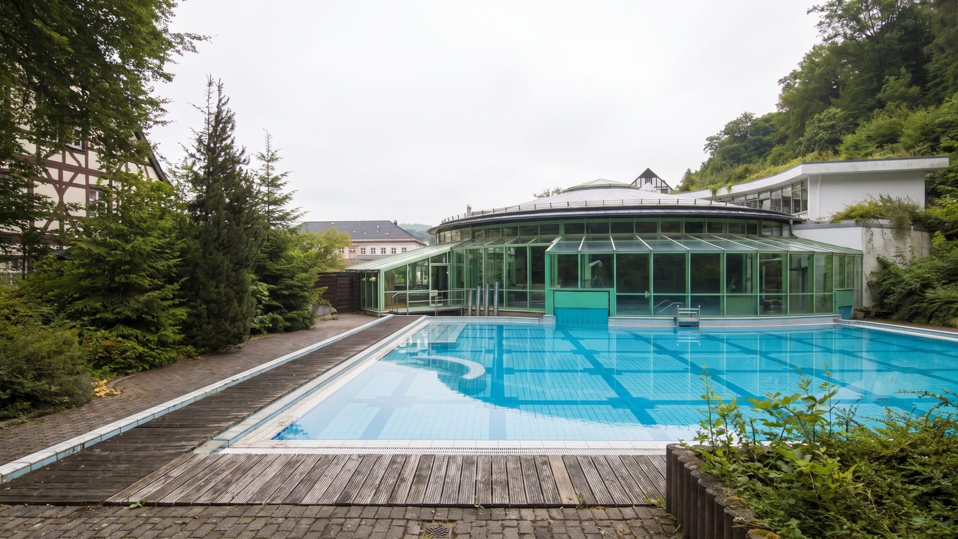 The outdoor pool of the Therme Miriquidi from the timber deck at the water's edge, the glazed bath hall beyond