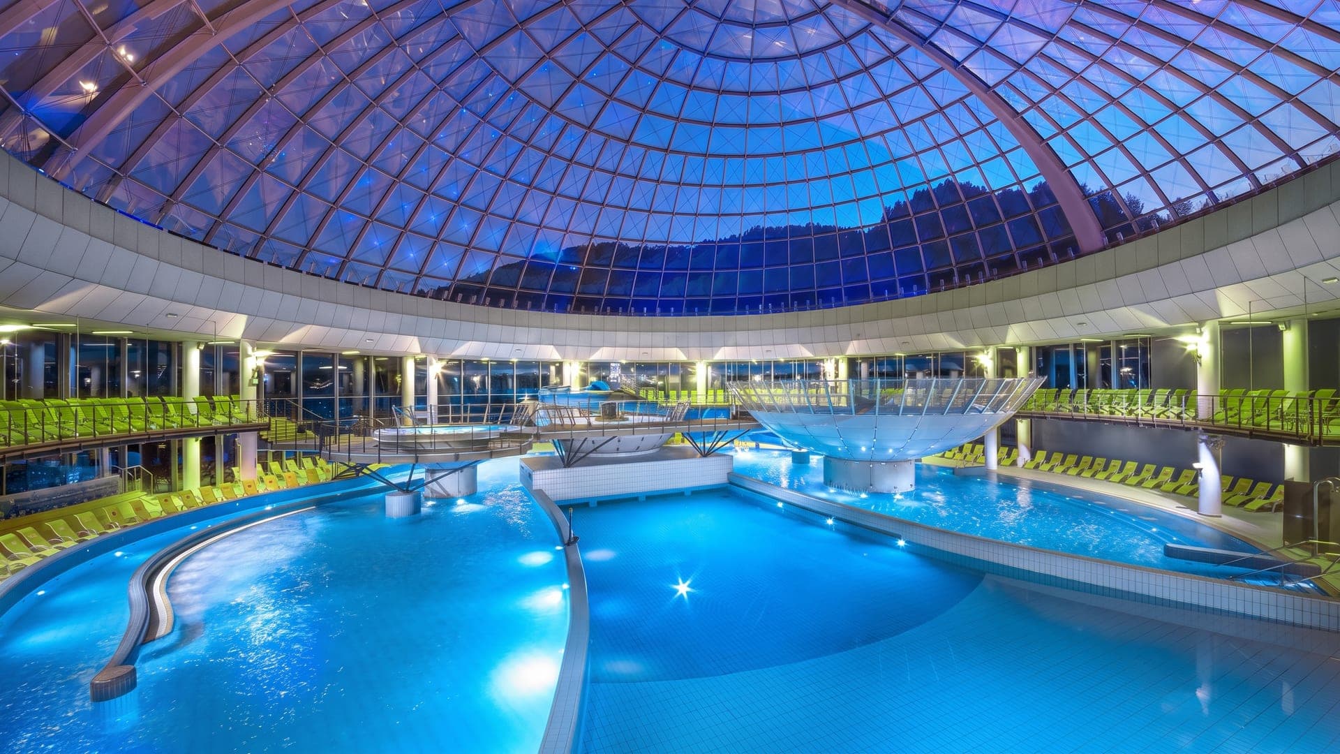 The bathing hall of Thermana Lasko under its blue glass dome, the pools below the curving glazed roof.