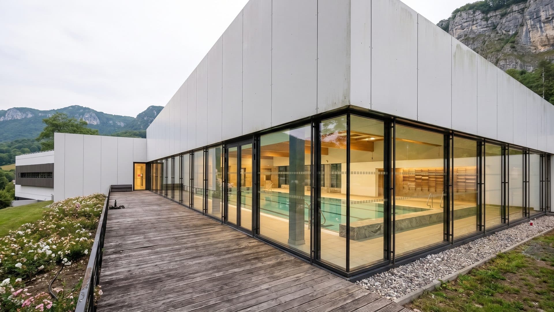 The glazed pool wing of ThermaSalina running away from the camera along its timber deck, with the limestone cliff rising behind