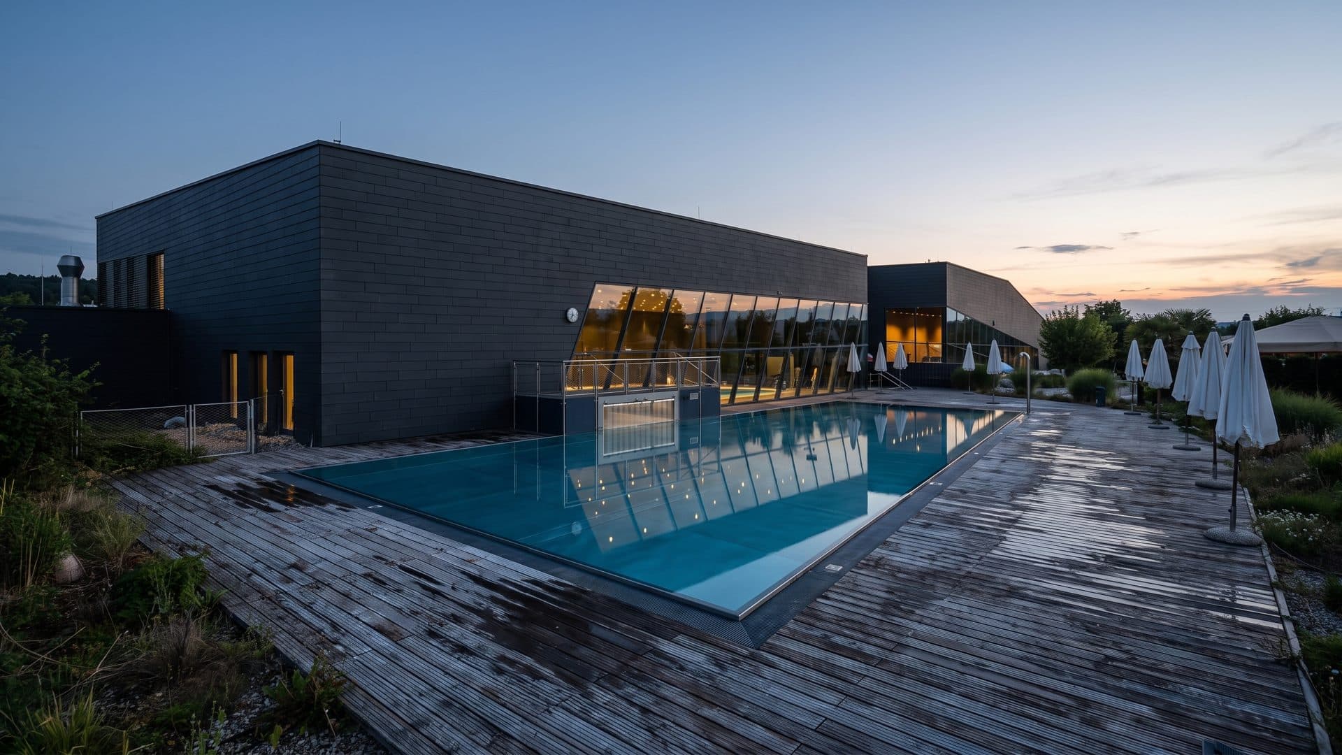 Therme Aqualux at dusk: the outdoor pool beside the dark modern bath building in Fohnsdorf.