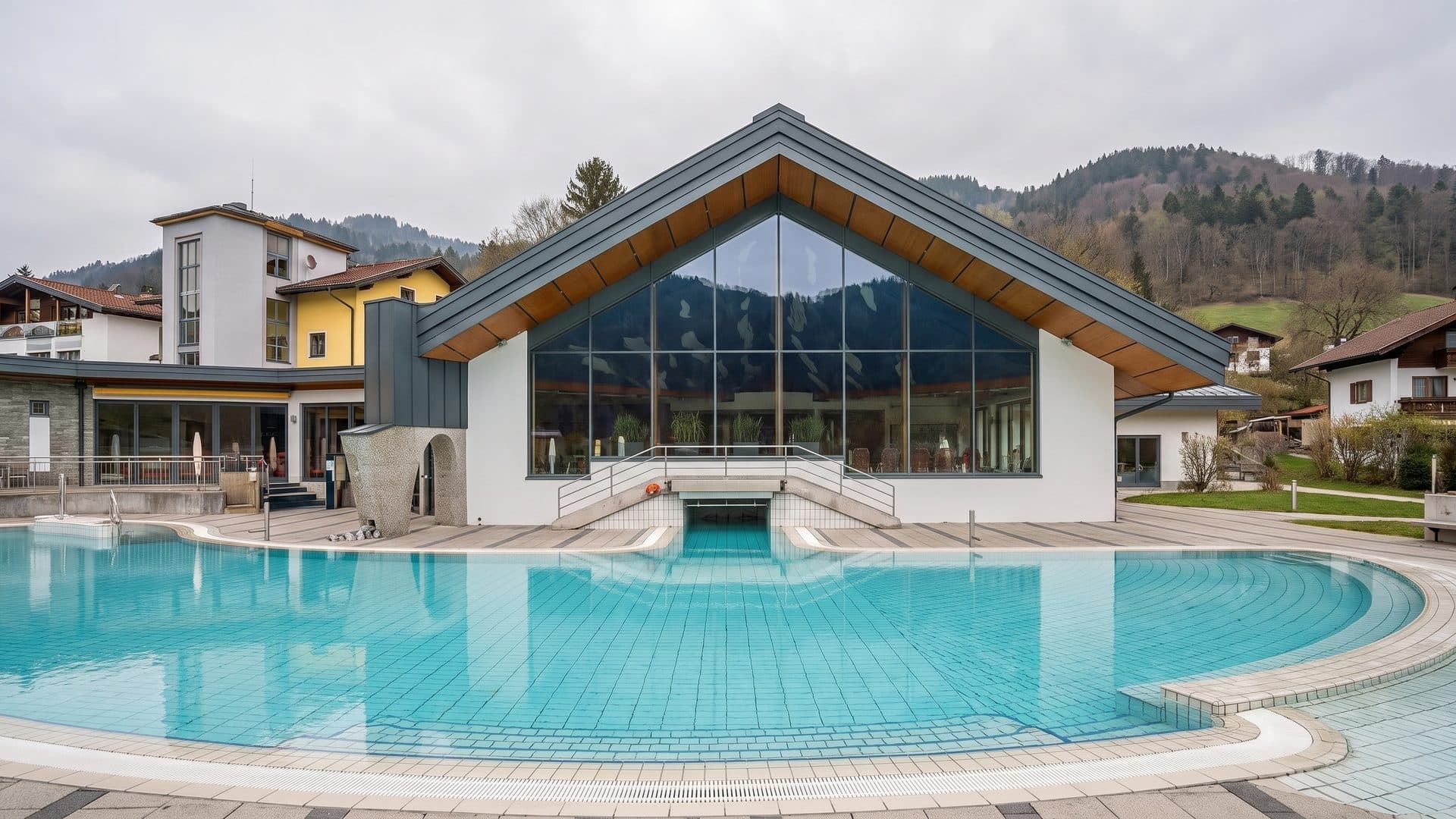 The glazed building of Therme Bad Vigaun with its outdoor pool and the hills behind