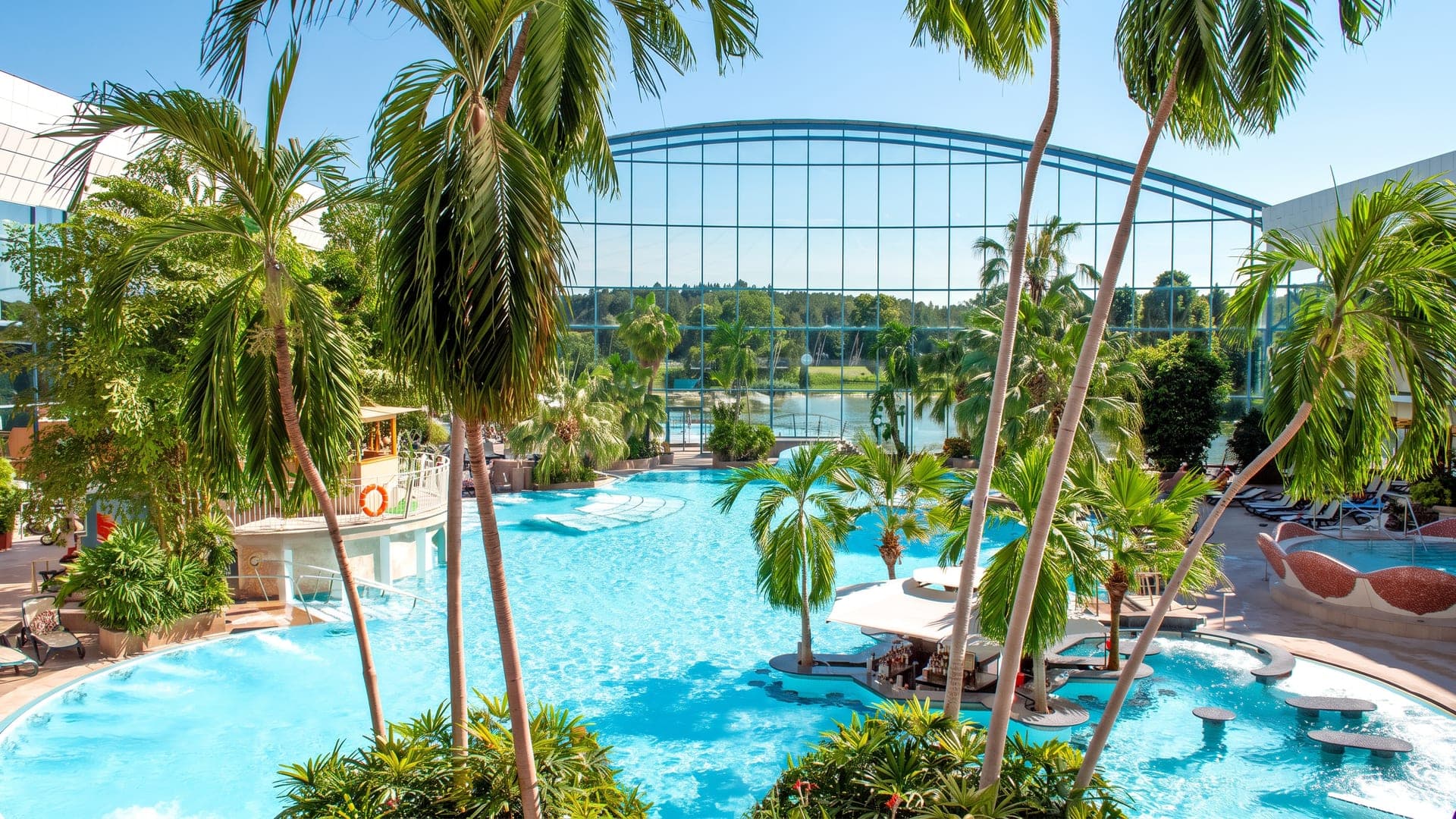 The bathing hall at Therme Bad Woerishofen, its pools under an arched glass roof among tall palms.
