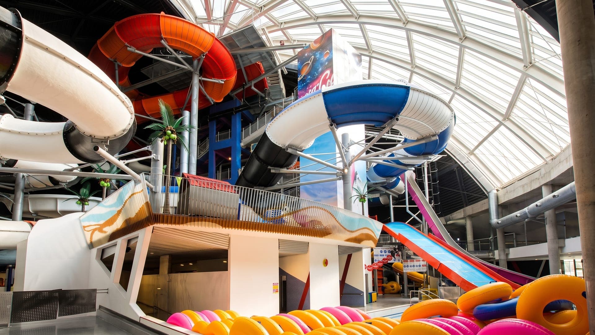 Slide tower of coloured tubes and stacked rings under a glazed dome