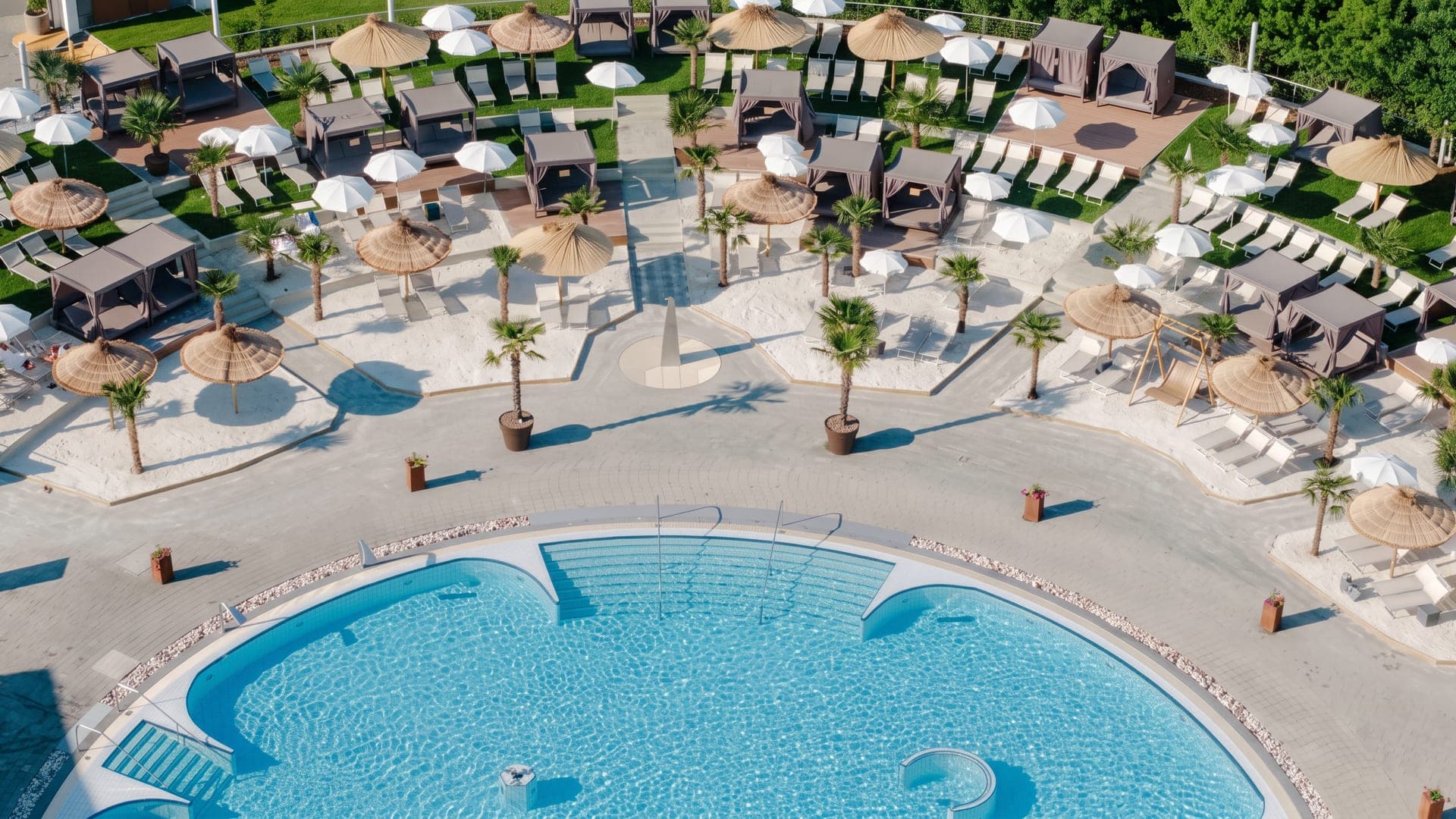 Aerial view of the sand-rimmed pool with planted palms, parasols and cabanas