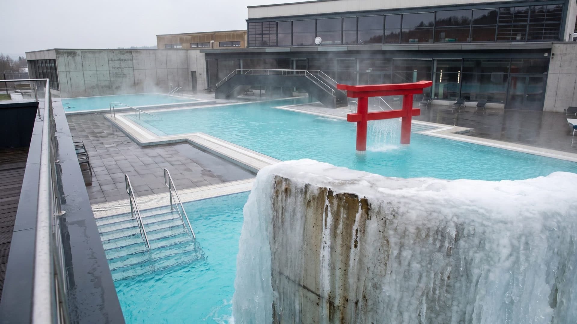 Steaming outdoor thermal pool with a red torii gate and a travertine-crusted fountain