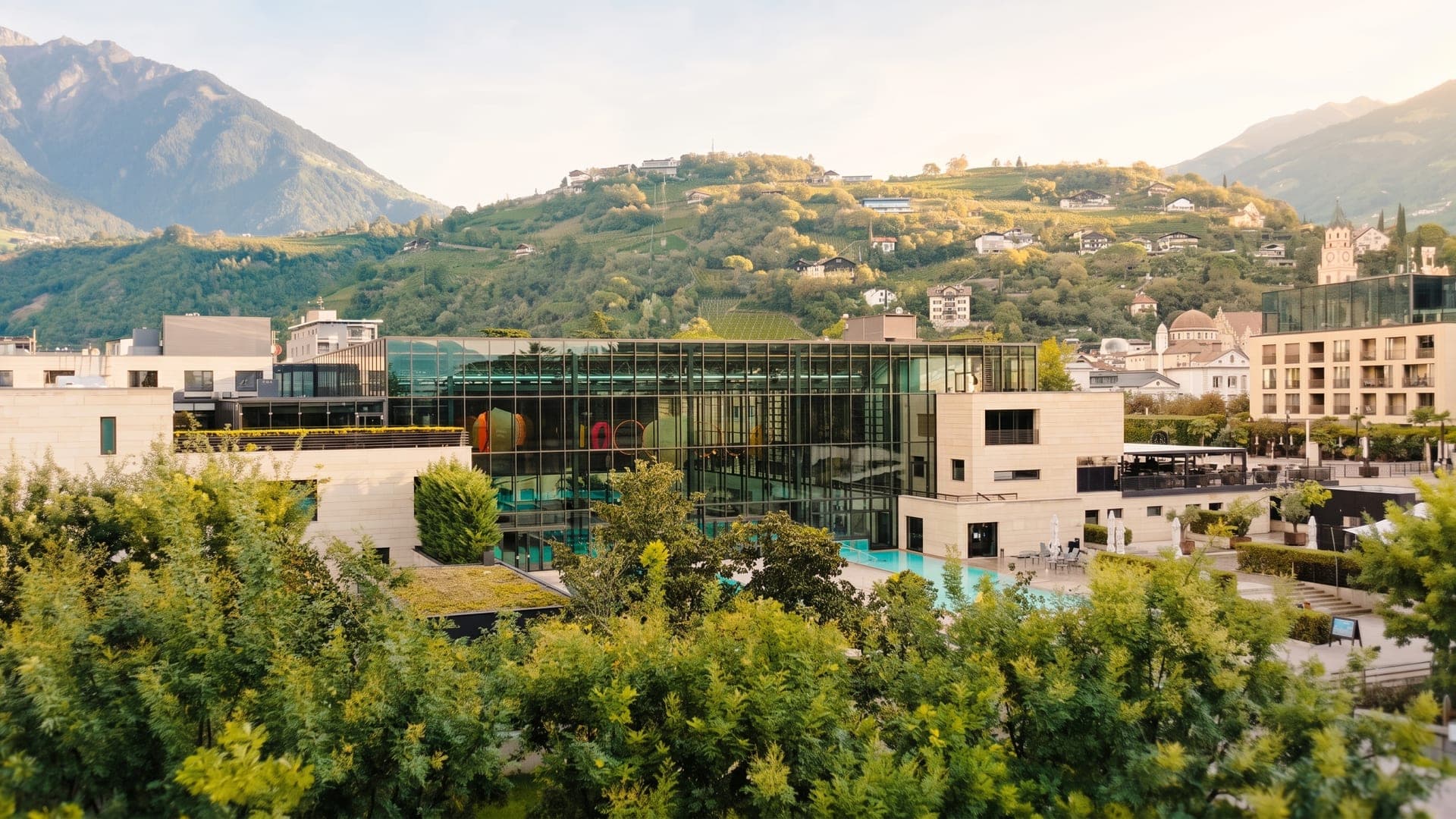 The glass cube of the baths among gardens, with vineyards and mountains behind