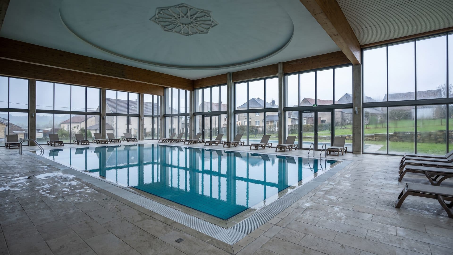 The indoor thermal pool hall at Therme Sankt Kathrein, glazed along one side under a shallow domed ceiling.