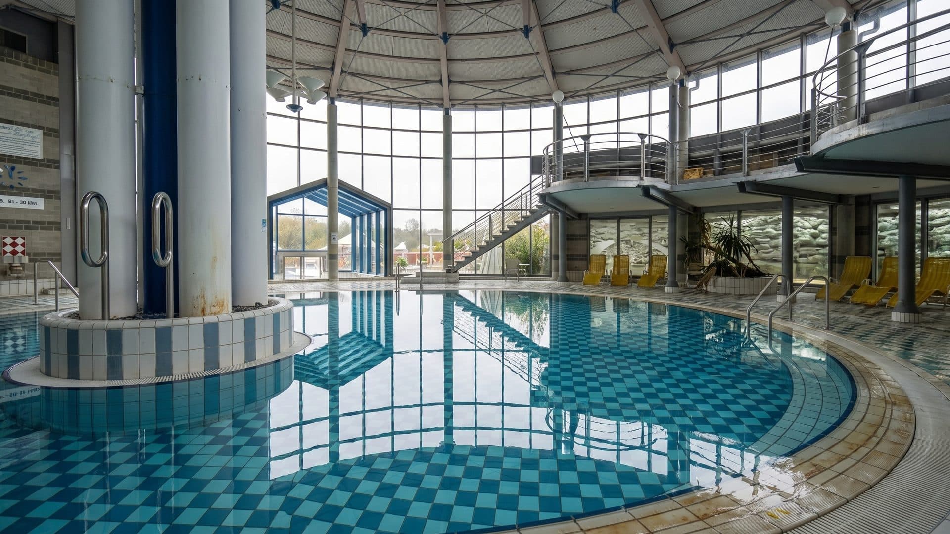 Round indoor thermal pool with a chequered tile floor, under a glazed rotunda roof