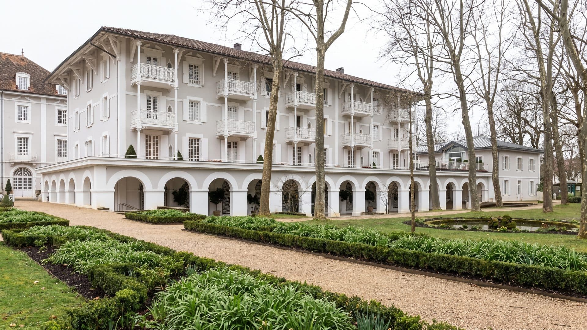 The white arcaded thermal building of Eugenie-les-Bains seen across its garden