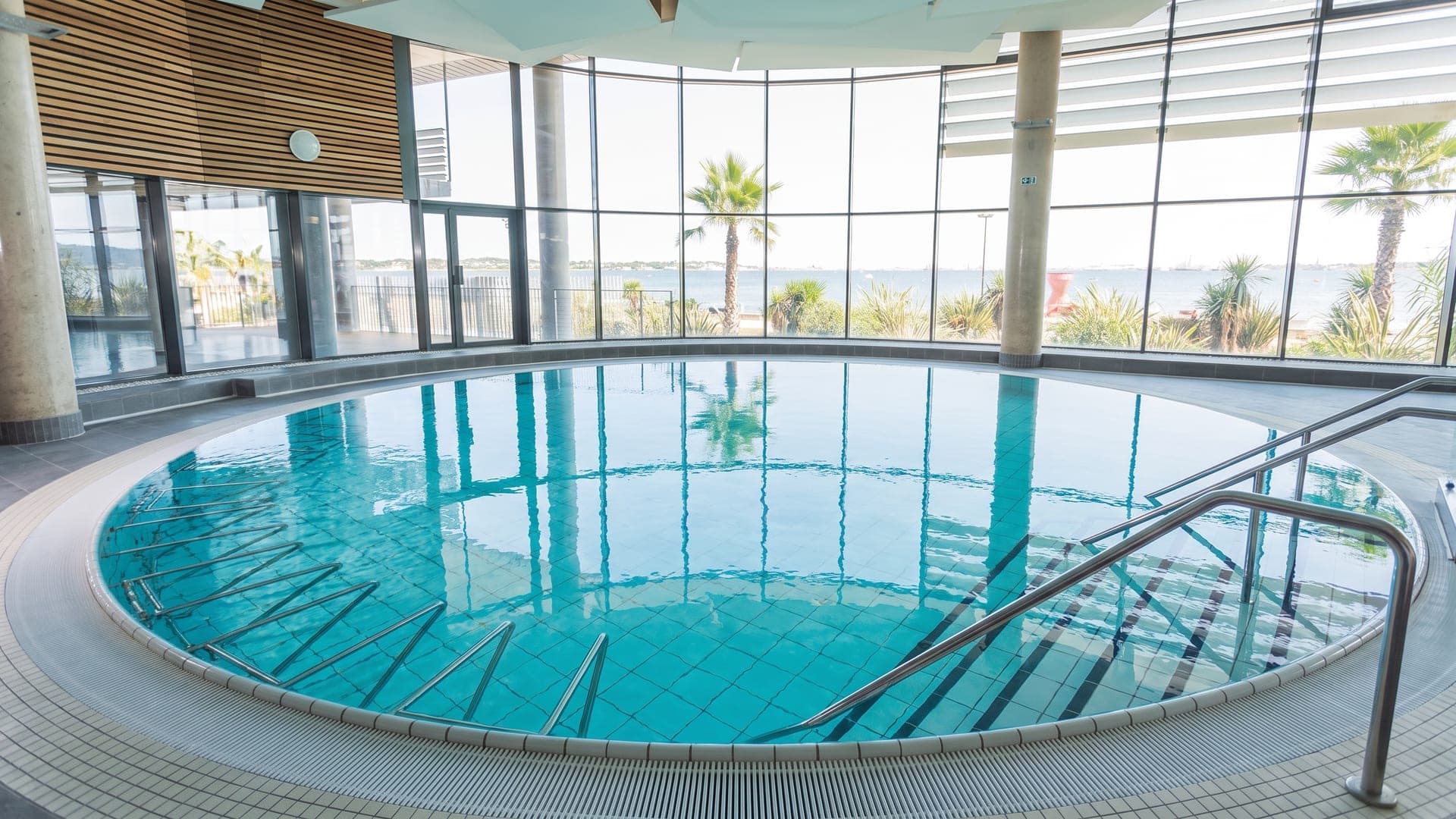 The circular indoor pool at the Thermes de Balaruc, its glass wall opening onto the Etang de Thau with palms along the shore.