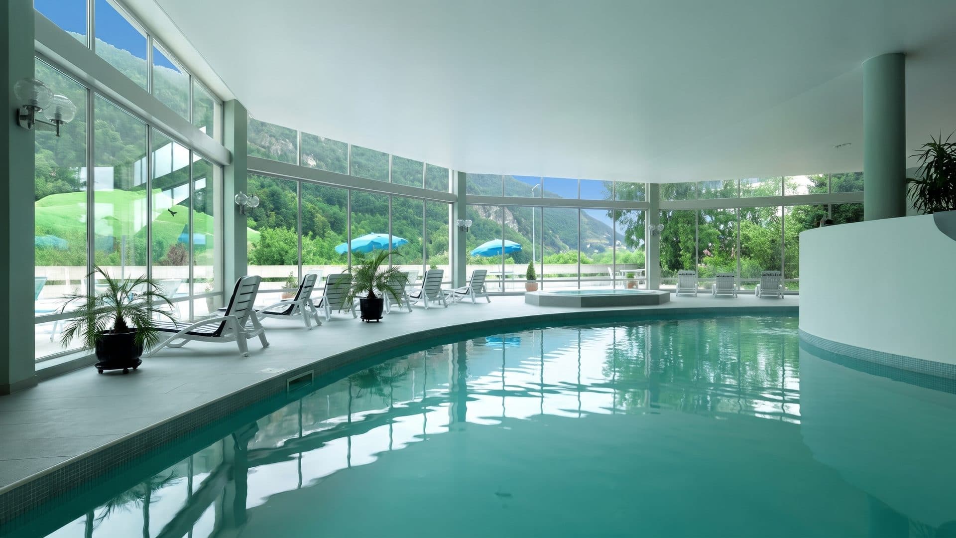 The indoor pool of the Thermes Regina along its glazed wall with the mountains beyond