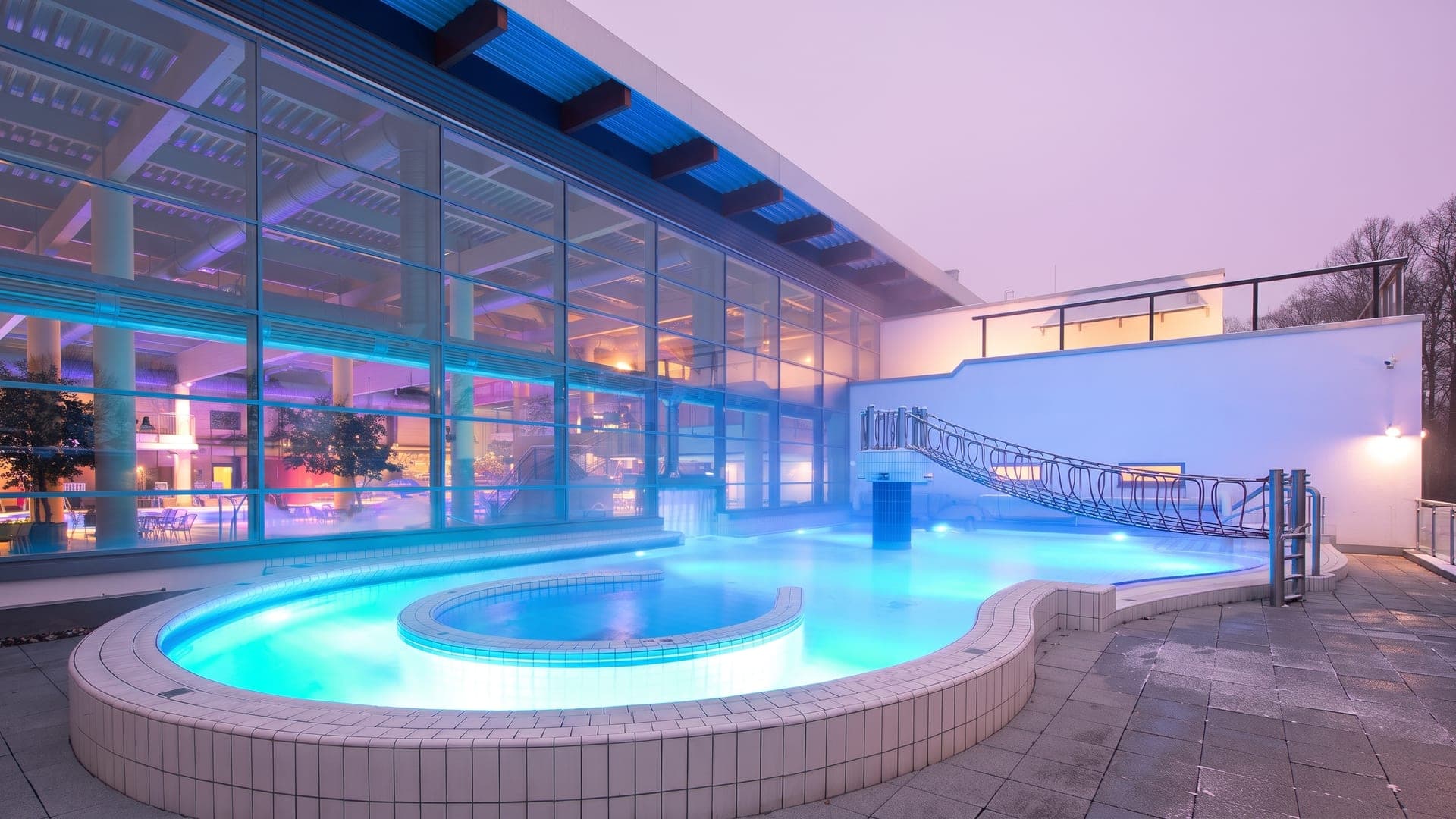 The outdoor pool at the Thueringentherme in Muehlhausen at dusk, in front of the lit glass hall.